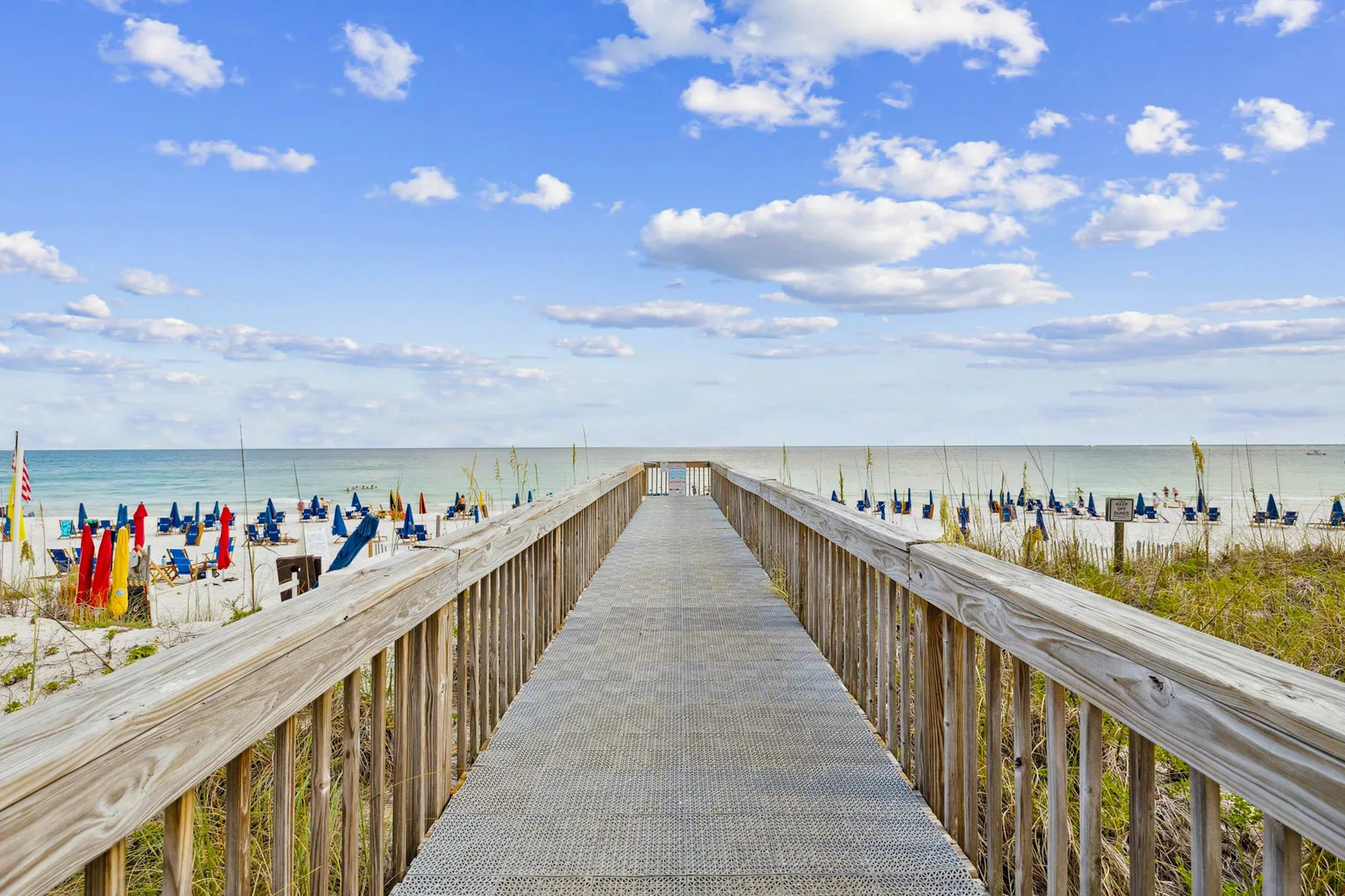 A wooden boardwalk crosses the beach toward the ocean under a partly cloudy sky.