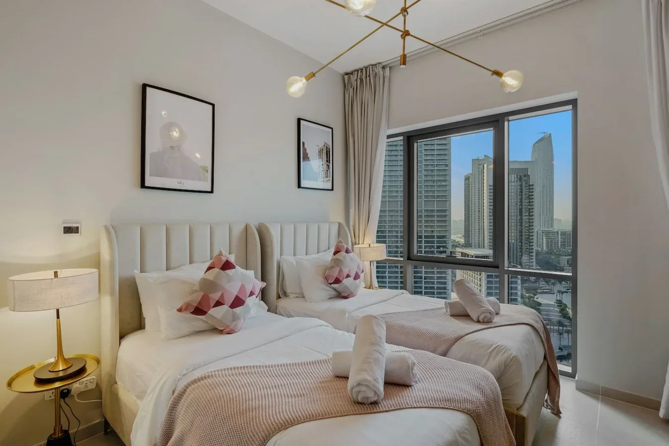 Un dormitorio luminoso con dos camas y grandes ventanas con vistas a edificios de la ciudad.