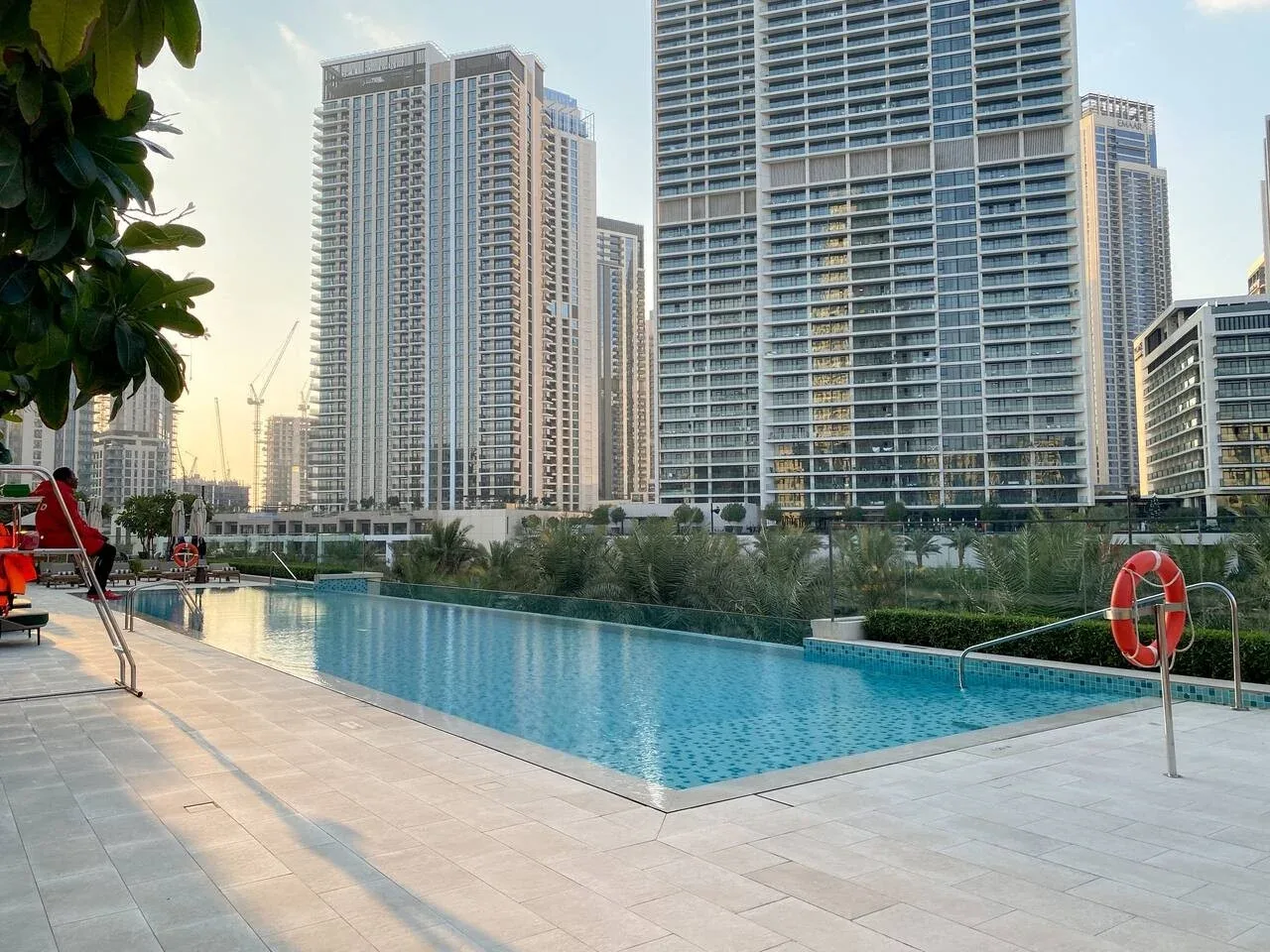 Una piscina al aire libre y una terraza pavimentada están frente a edificios altos.