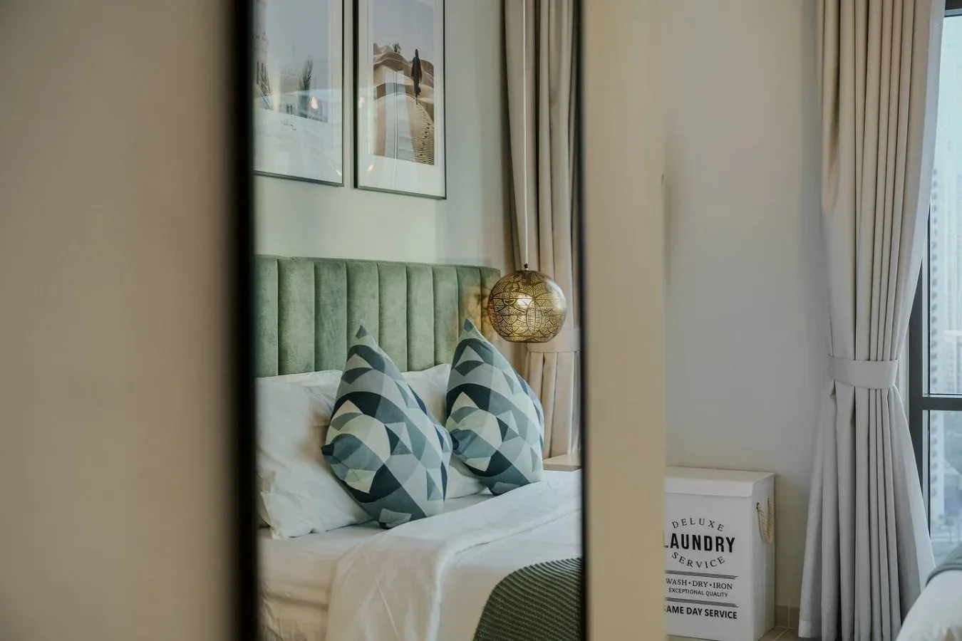 Un dormitorio con una cama, cojines estampados, cuadros enmarcados y cortinas junto a una ventana.