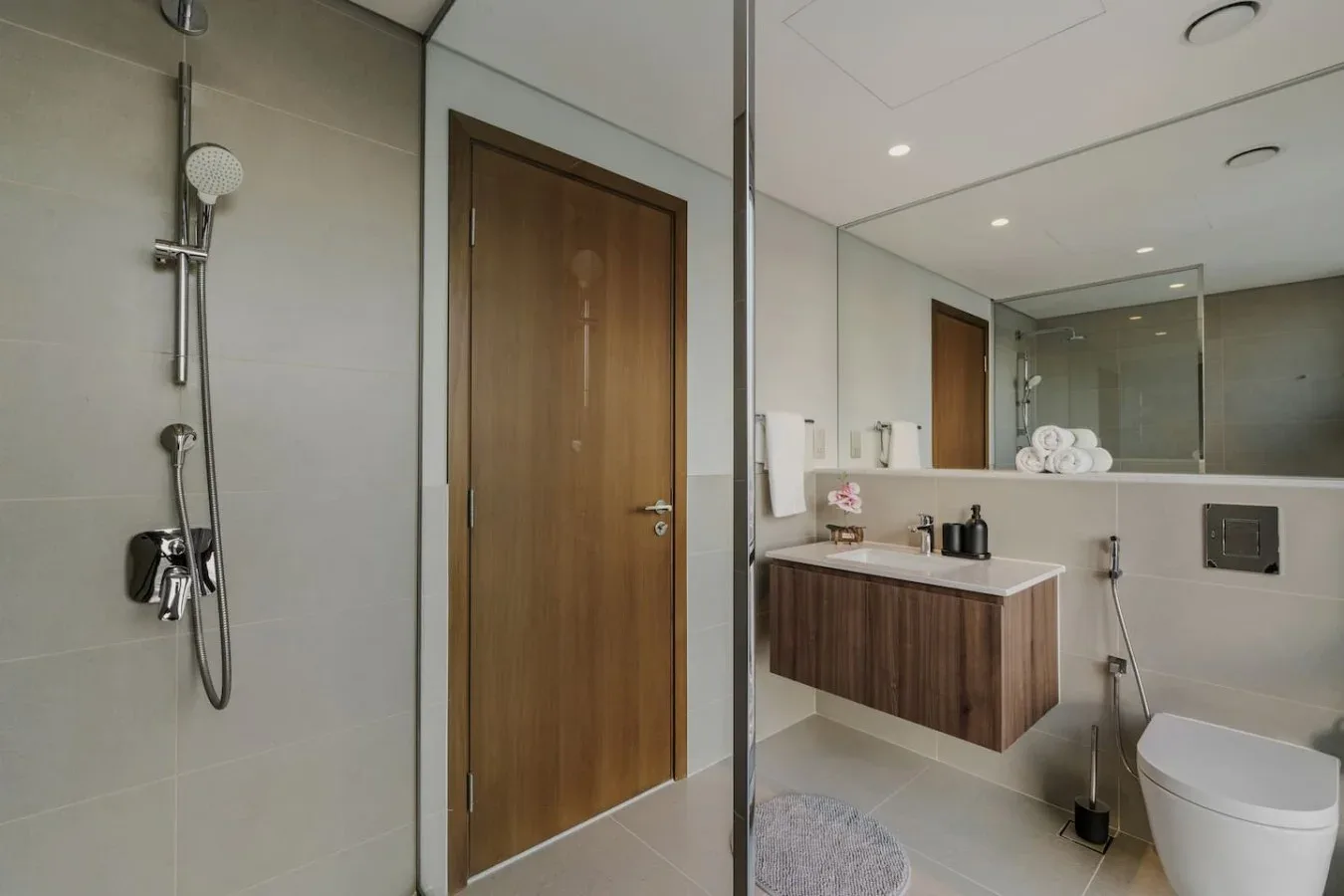 Un baño moderno con ducha de vidrio, mueble de madera y sanitario.