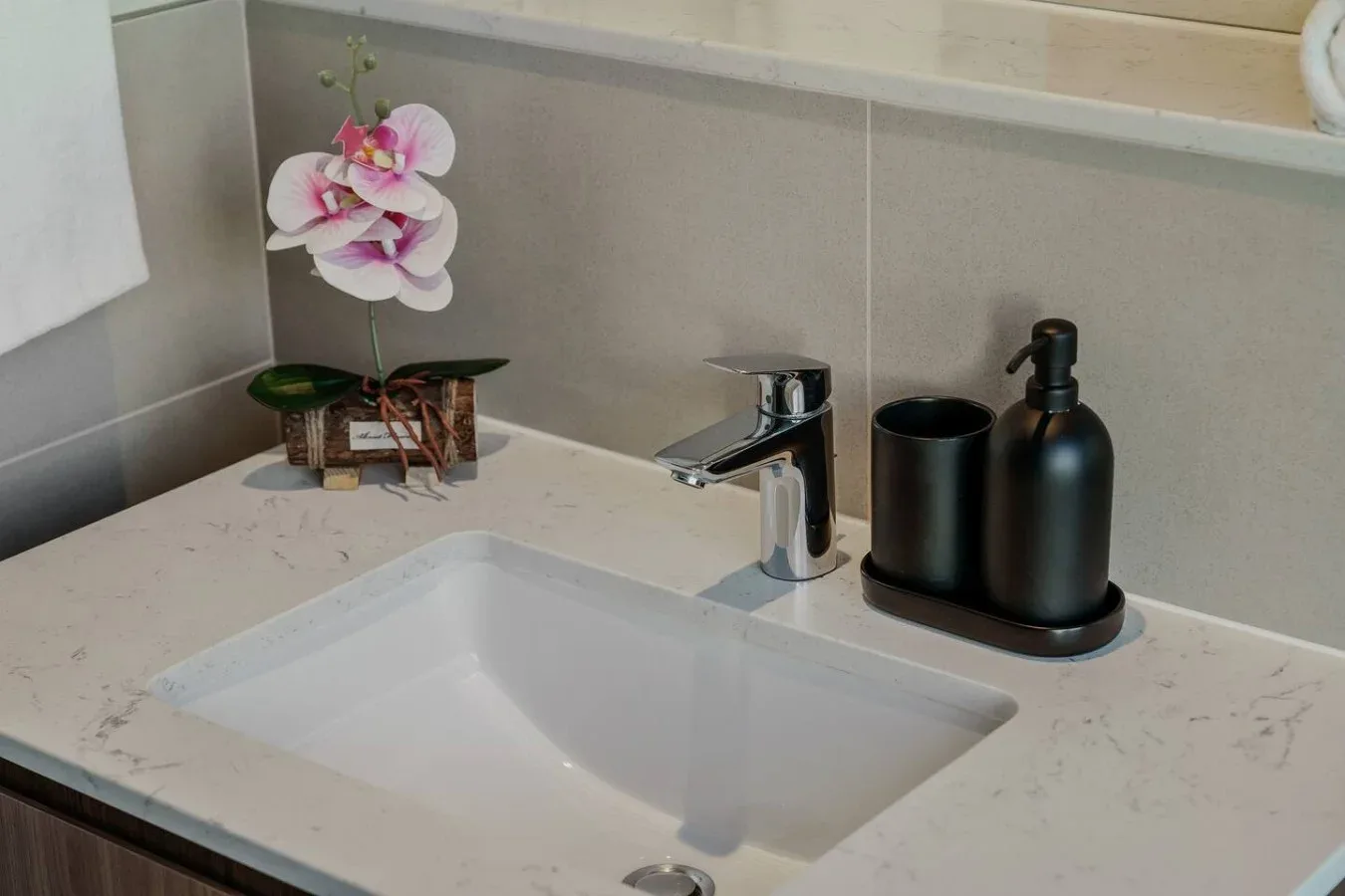 Un lavabo de baño con grifo cromado y accesorios negros sobre la encimera.