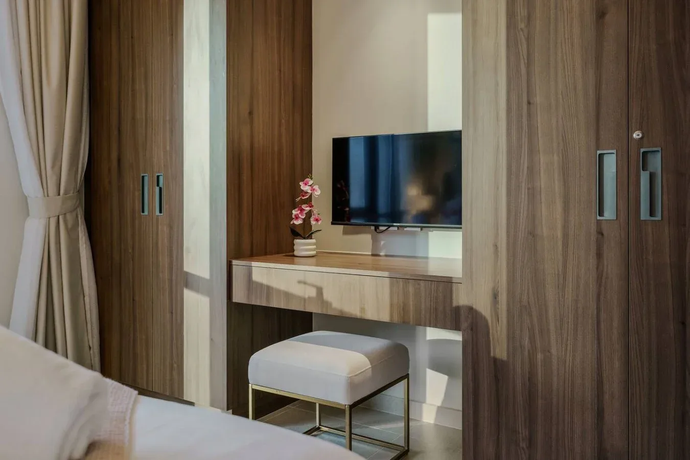 Un tocador de dormitorio con televisor, un asiento acolchado y armarios de madera.
