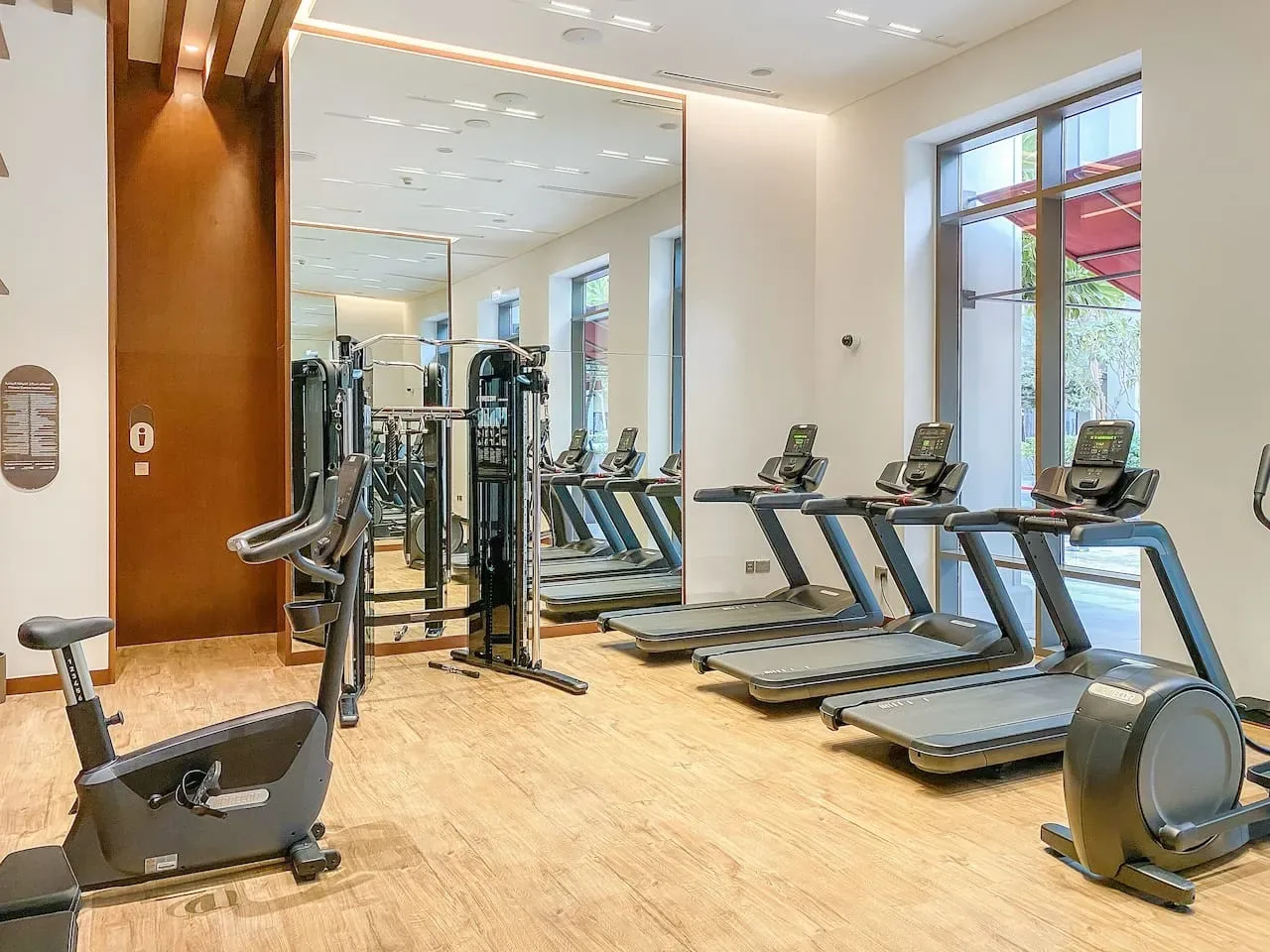 Una sala de fitness con cintas de correr y máquinas de ejercicio junto a una gran pared de espejo.