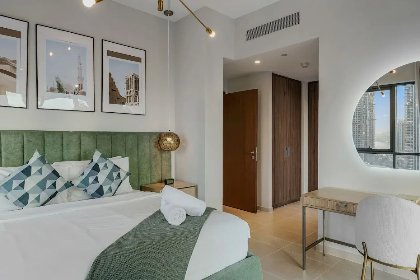 Un dormitorio con una cama, un cabecero verde tapizado y láminas enmarcadas en la pared.