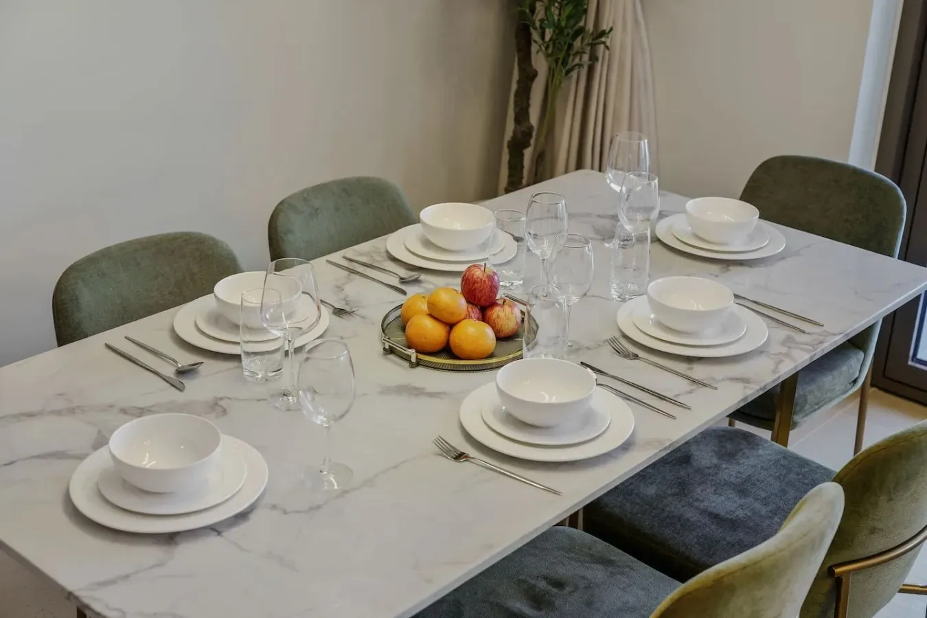 Una mesa de comedor está preparada con platos y un cuenco de fruta.