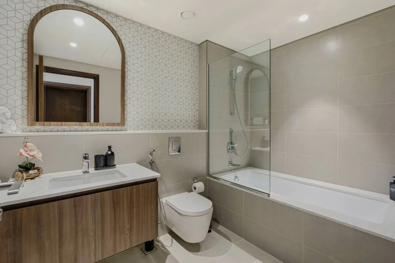Un baño revestido de azulejos con lavabo, inodoro y bañera detrás de una mampara de vidrio.