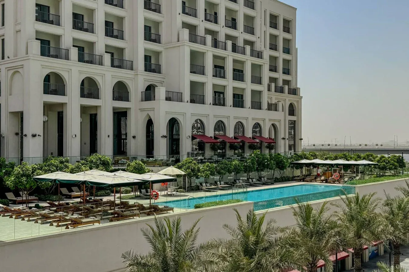 Un edificio hotelero da a una piscina al aire libre y varias filas de tumbonas.