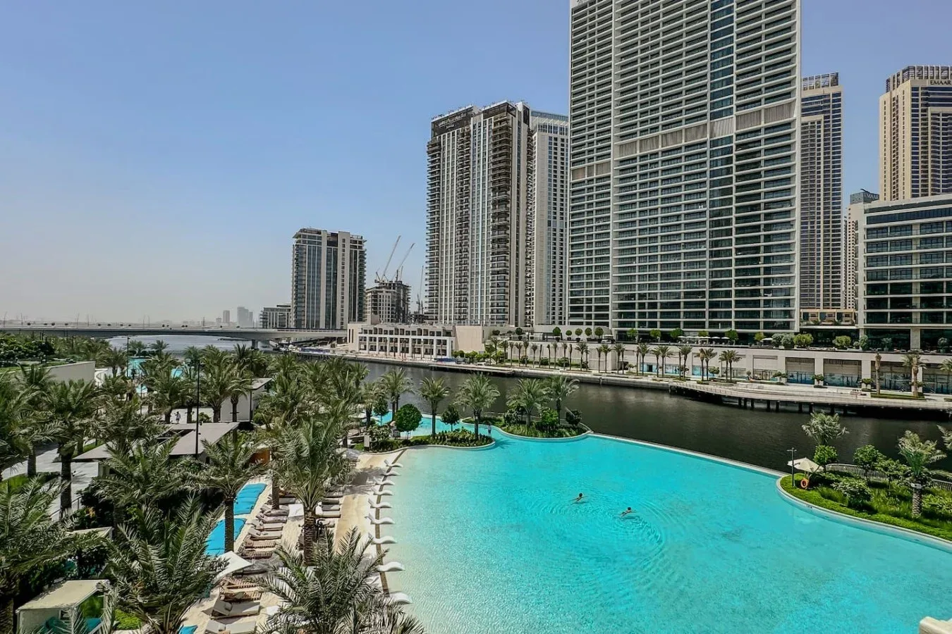 Una gran piscina al aire libre está rodeada de jardines y edificios altos.