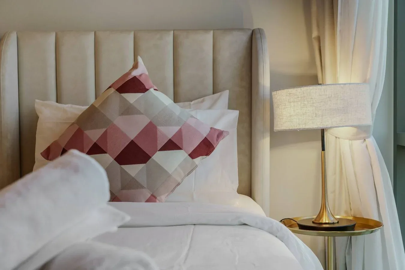Una cama bien tendida con cojines estampados está junto a una lámpara encendida.