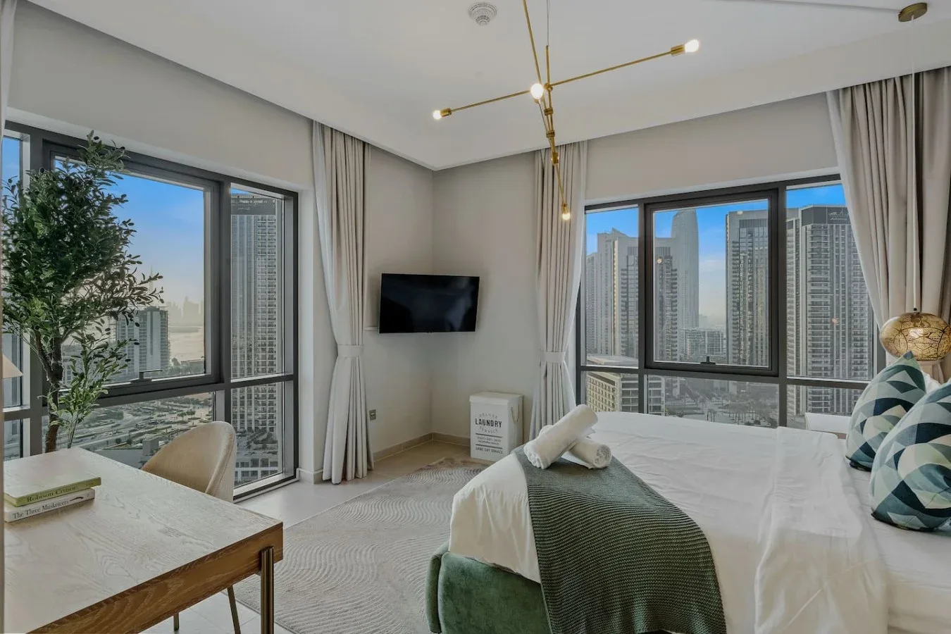 Un dormitorio luminoso con una cama junto a grandes ventanas con vistas a edificios de la ciudad.