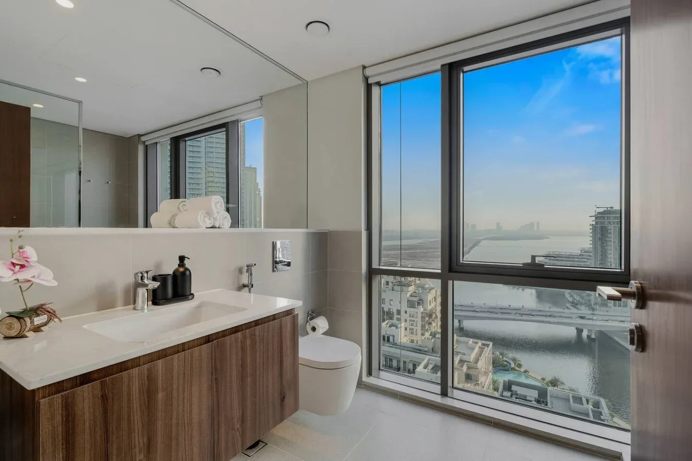 Un baño moderno con tocador, inodoro y amplios ventanales con vistas a la ciudad.
