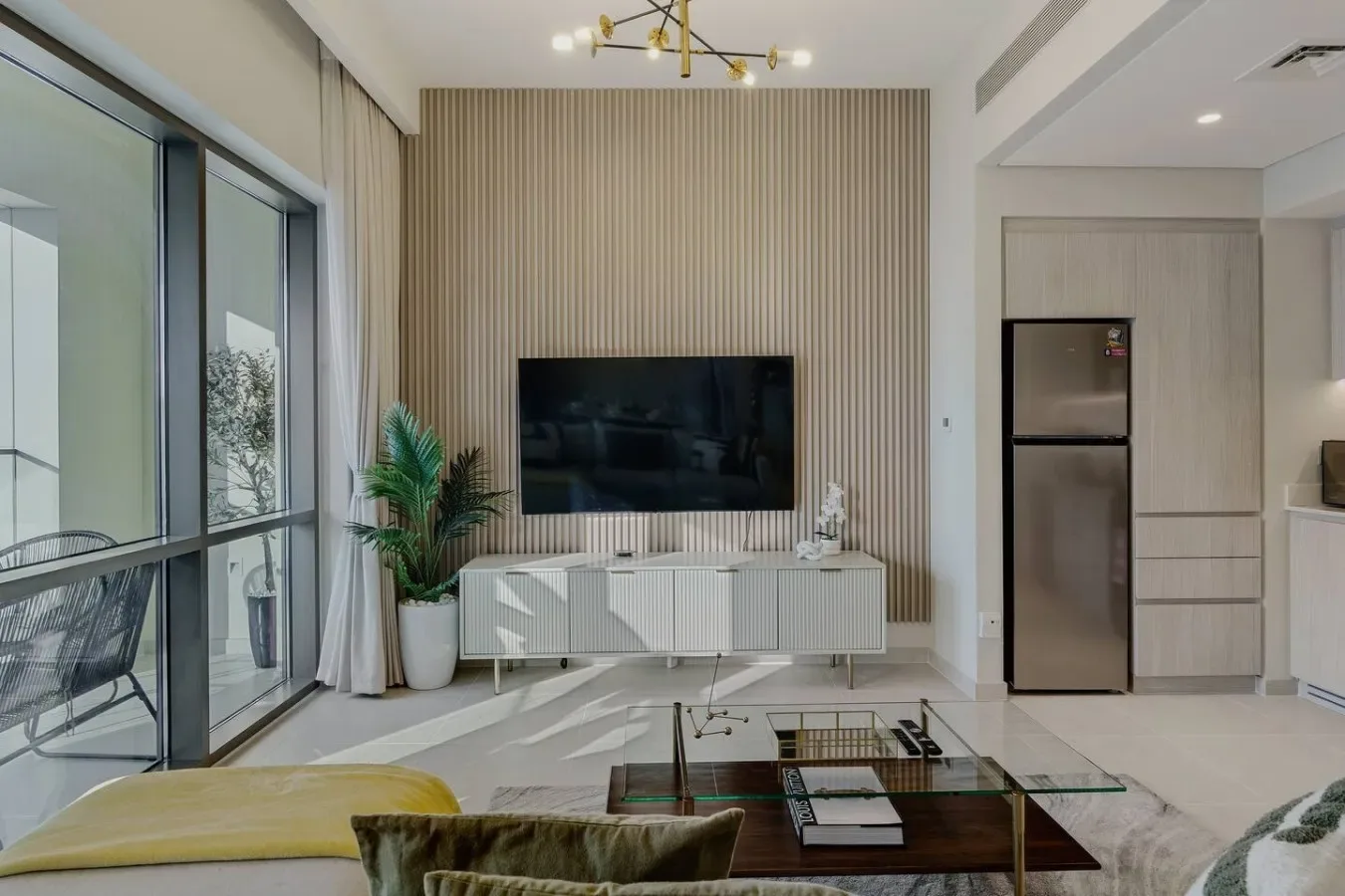 Una sala luminosa con un televisor en la pared y una cocina contigua.