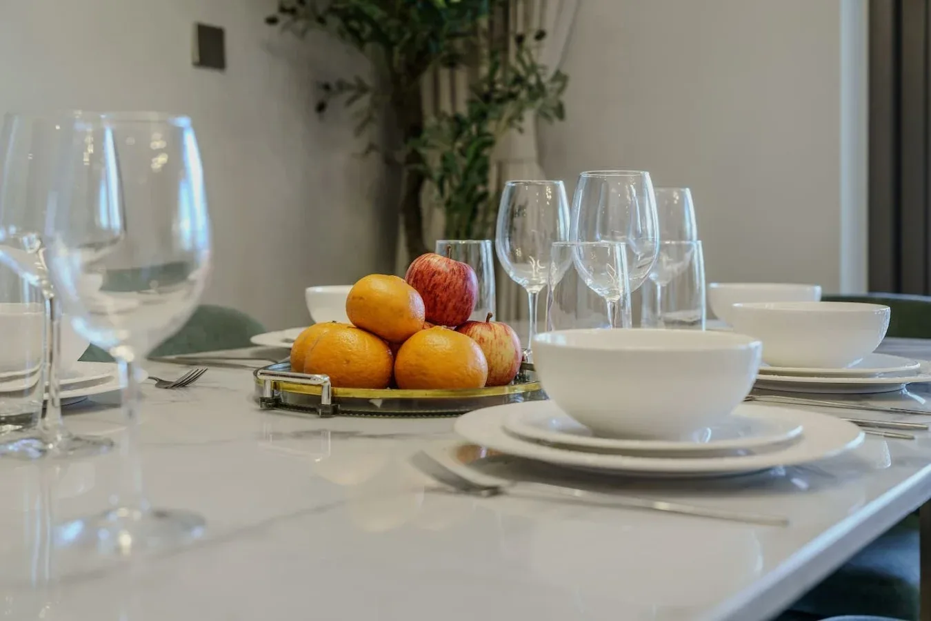 Una mesa de comedor está puesta con platos, copas y una fuente de fruta.