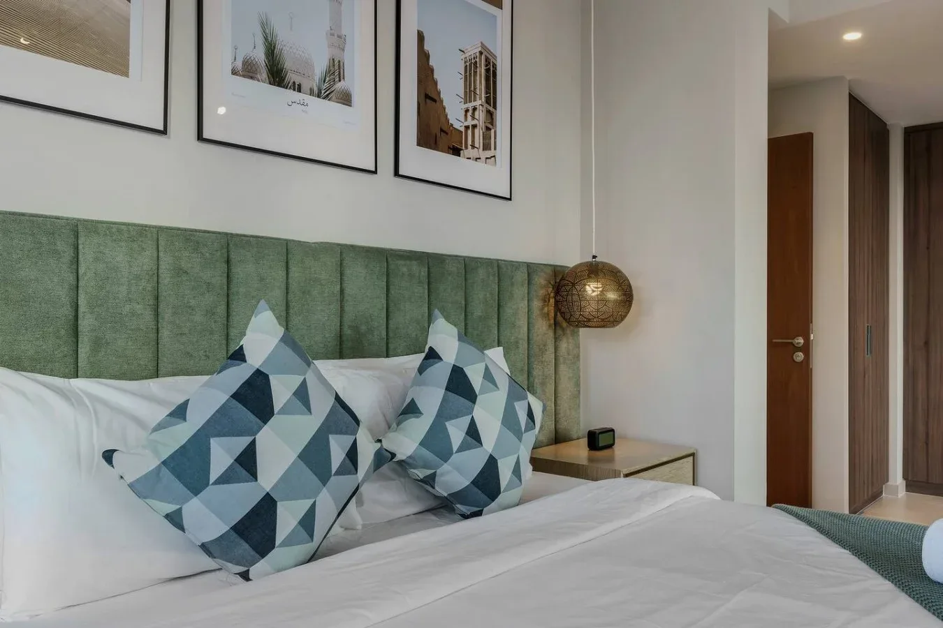Un dormitorio con una cama, cojines geométricos y cuadros enmarcados sobre el cabecero.