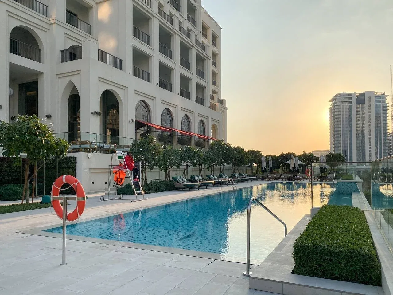 Una piscina al aire libre junto a un edificio moderno de varios pisos al atardecer.