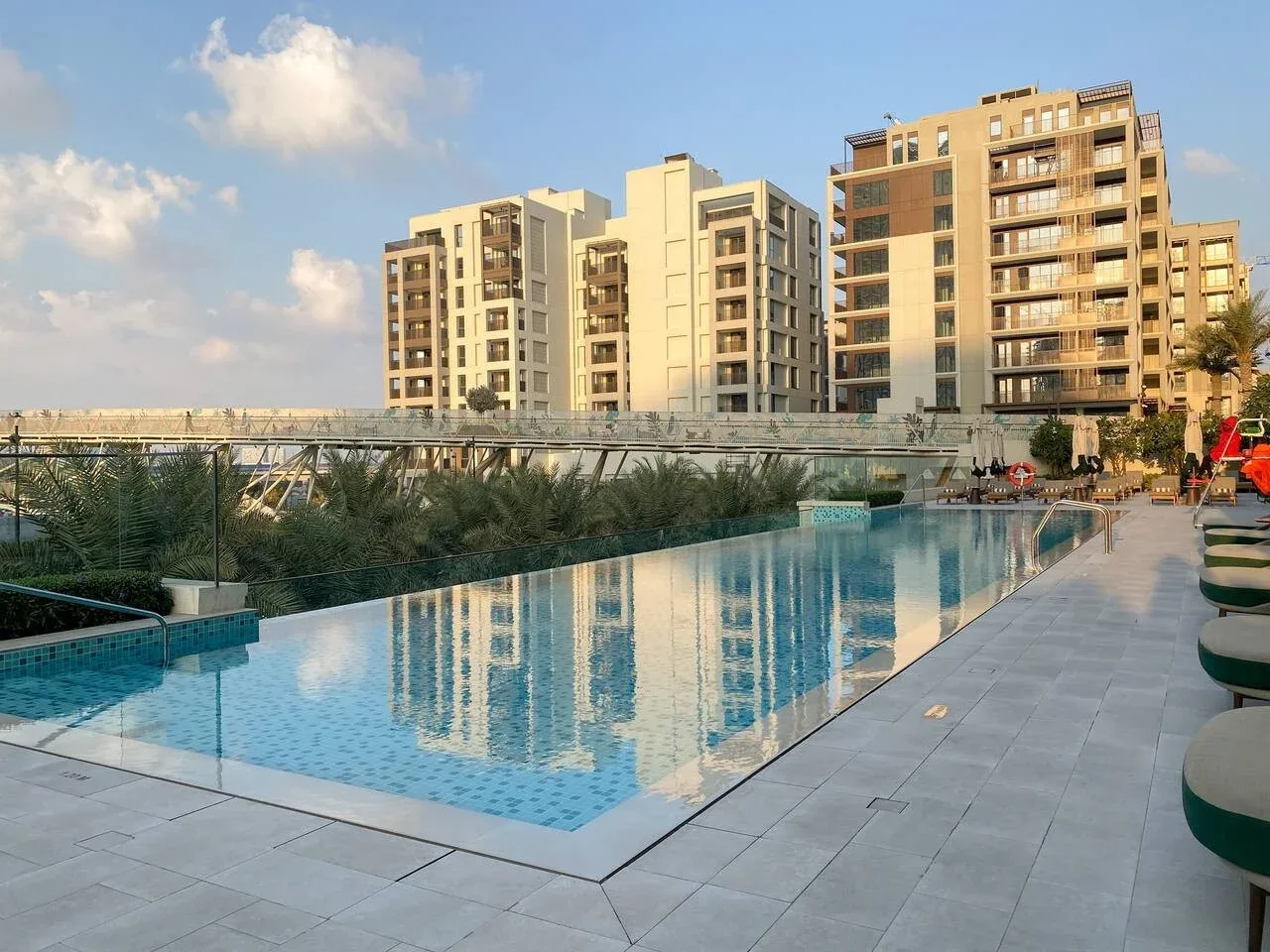 Una piscina exterior junto a edificios de apartamentos, con una terraza pavimentada y vegetación.