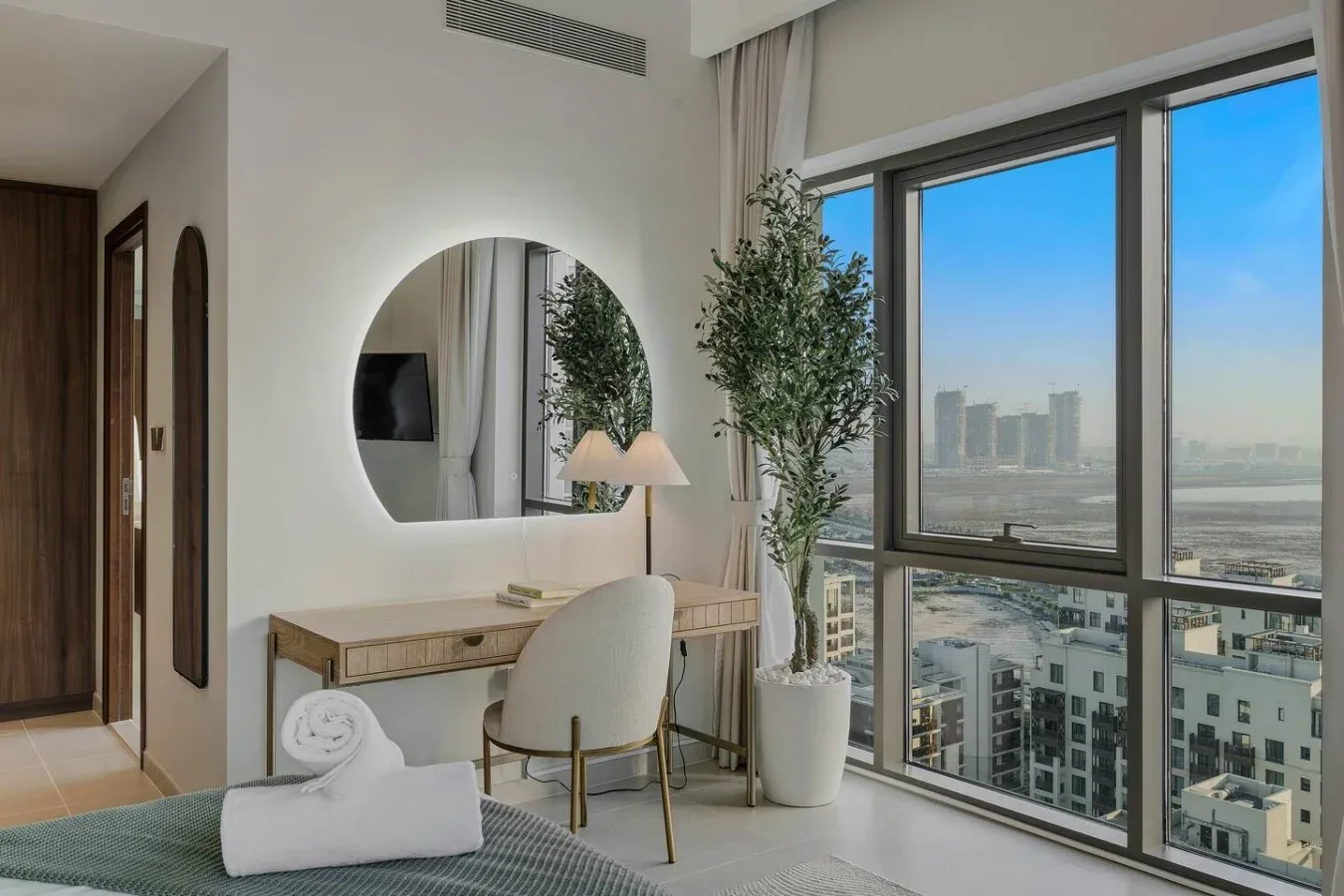 Un tocador y una zona de asientos en el dormitorio están junto a grandes ventanas con vistas a la ciudad.