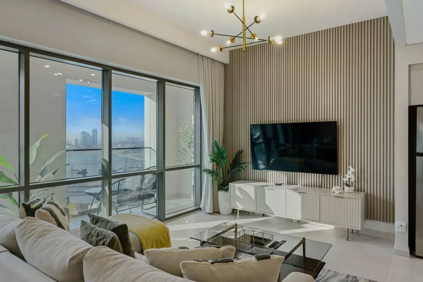 Una sala de estar moderna con asientos, un televisor de pared y grandes ventanales.