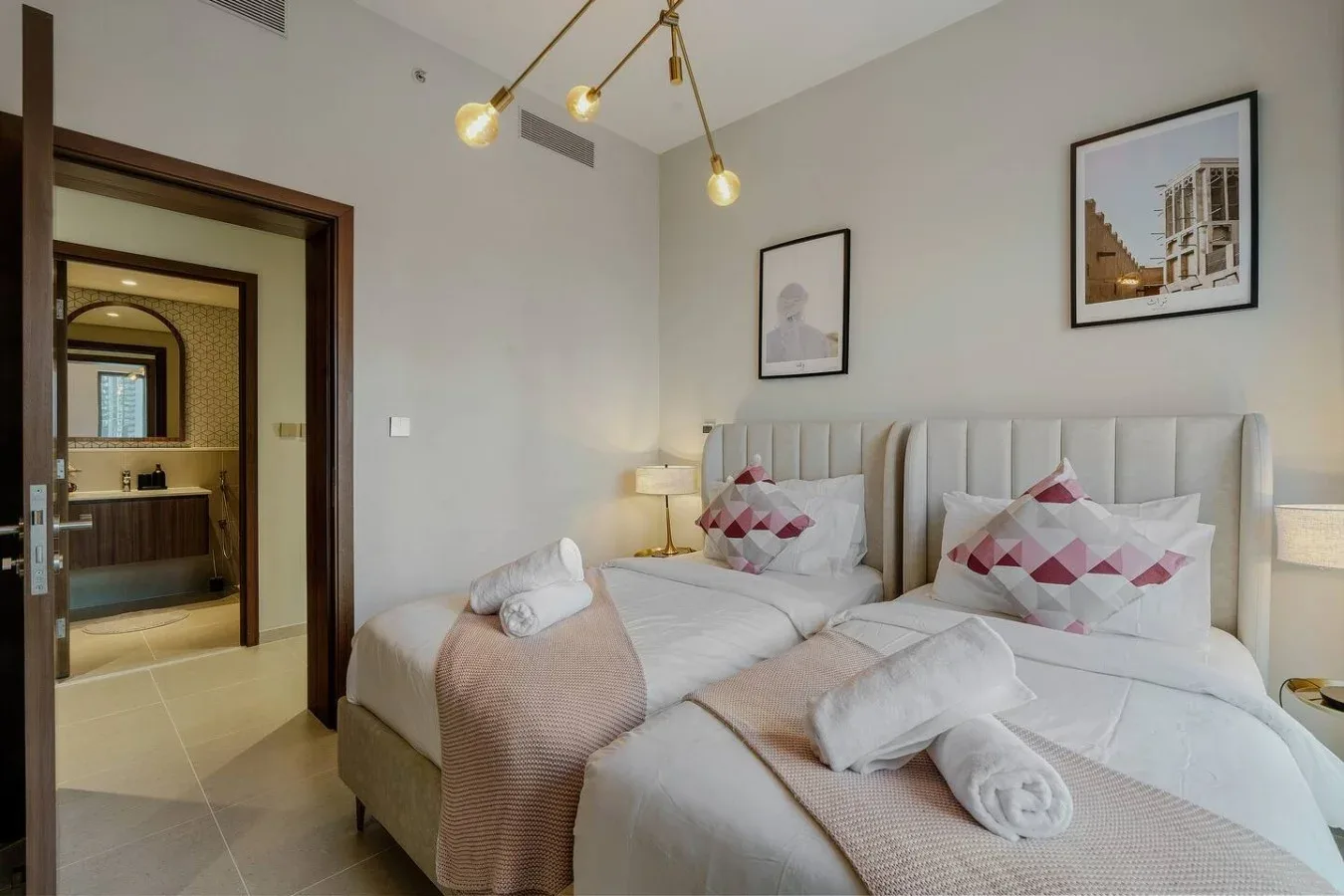 Un dormitorio luminoso con dos camas, arregladas con ropa de cama blanca y cojines estampados.