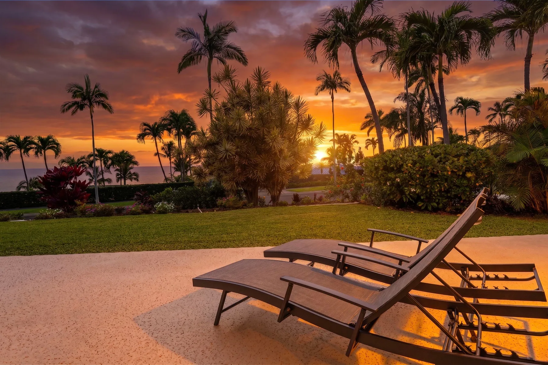 Outdoor seating beside a lawn, with palm trees silhouetted against a sunset.