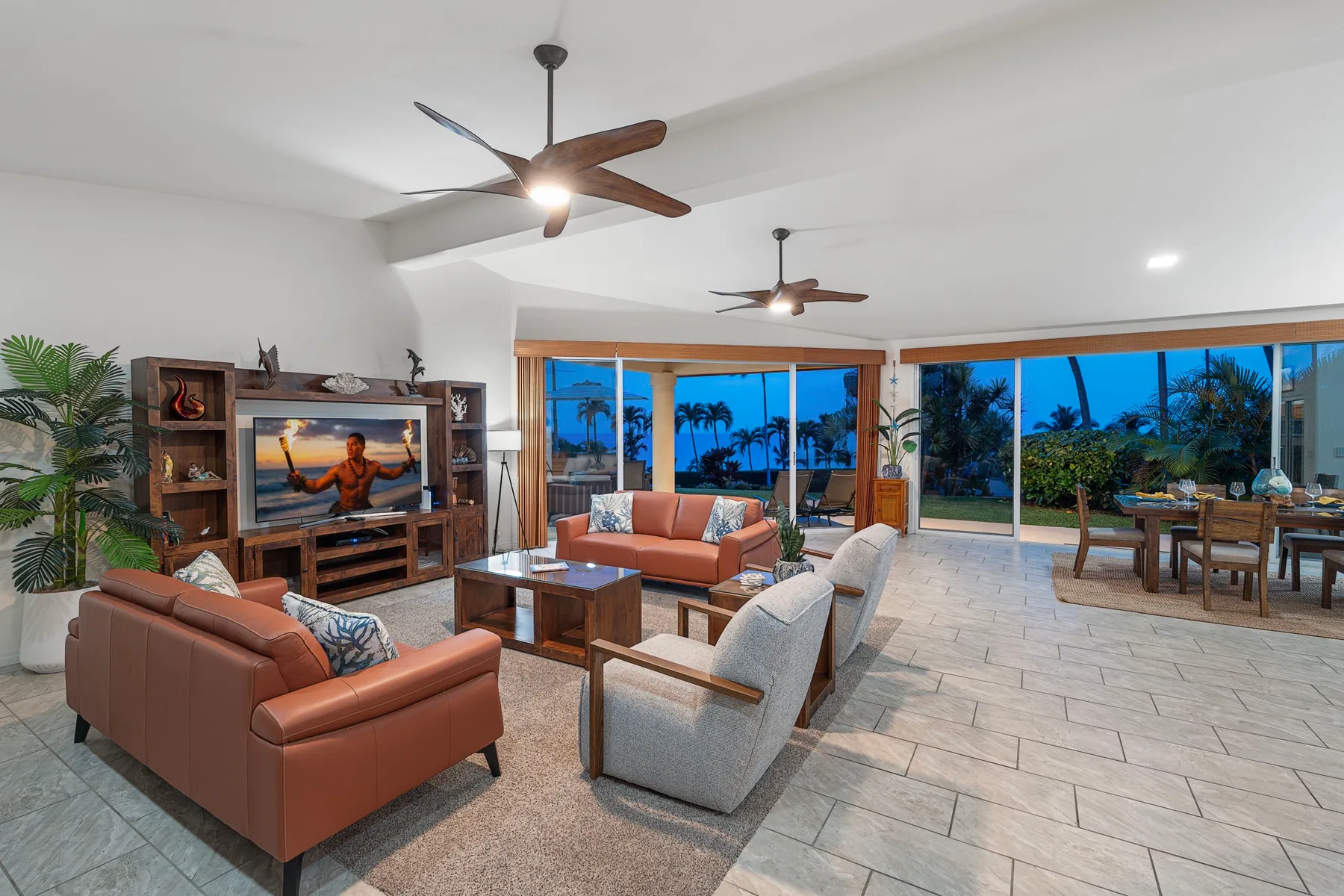 A bright living room with seating, a television, and wide windows overlooking greenery.