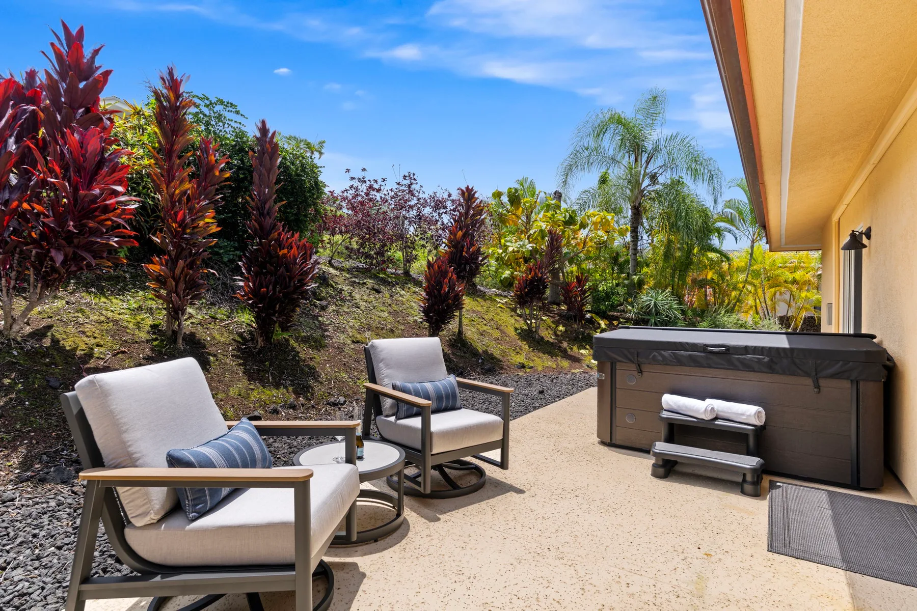 An outdoor patio with cushioned seating and a hot tub beside landscaped plants.