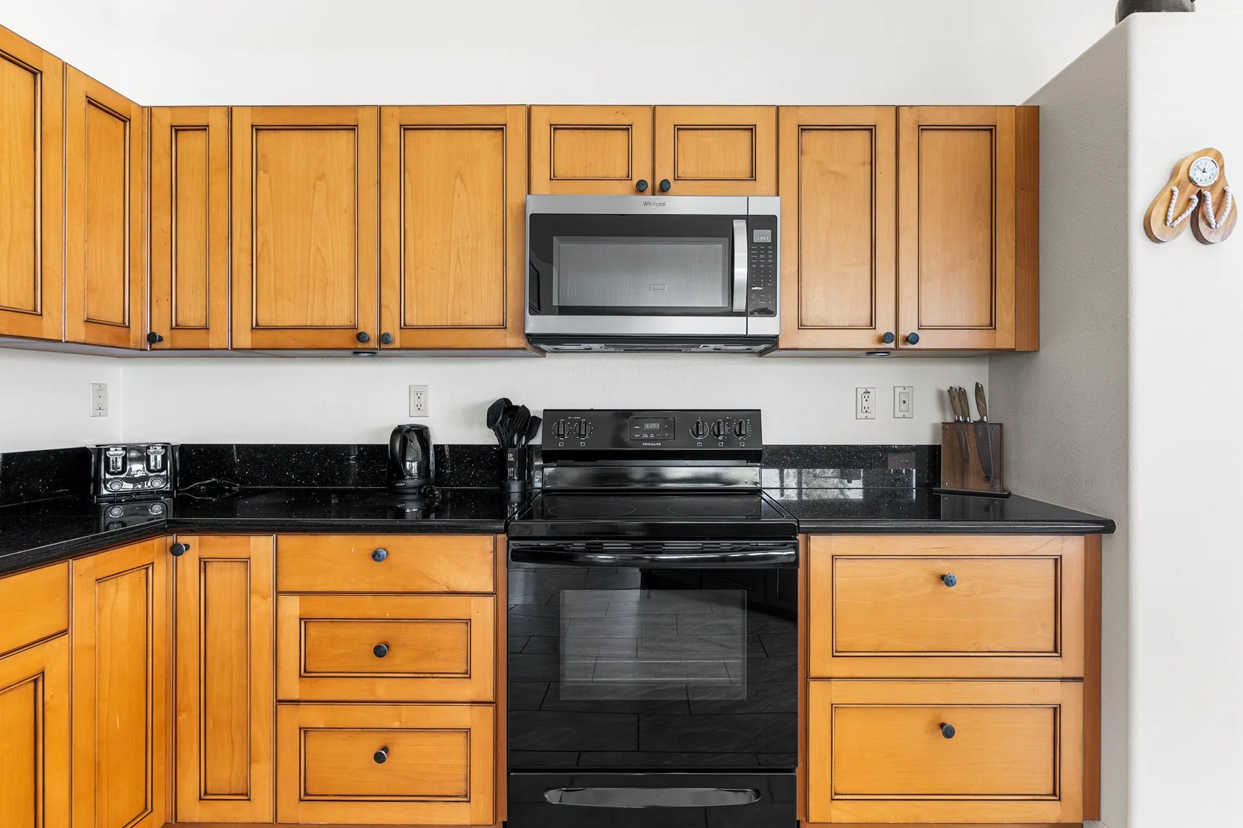 A kitchen with wooden cabinets, dark countertops, and a stove beneath a microwave.