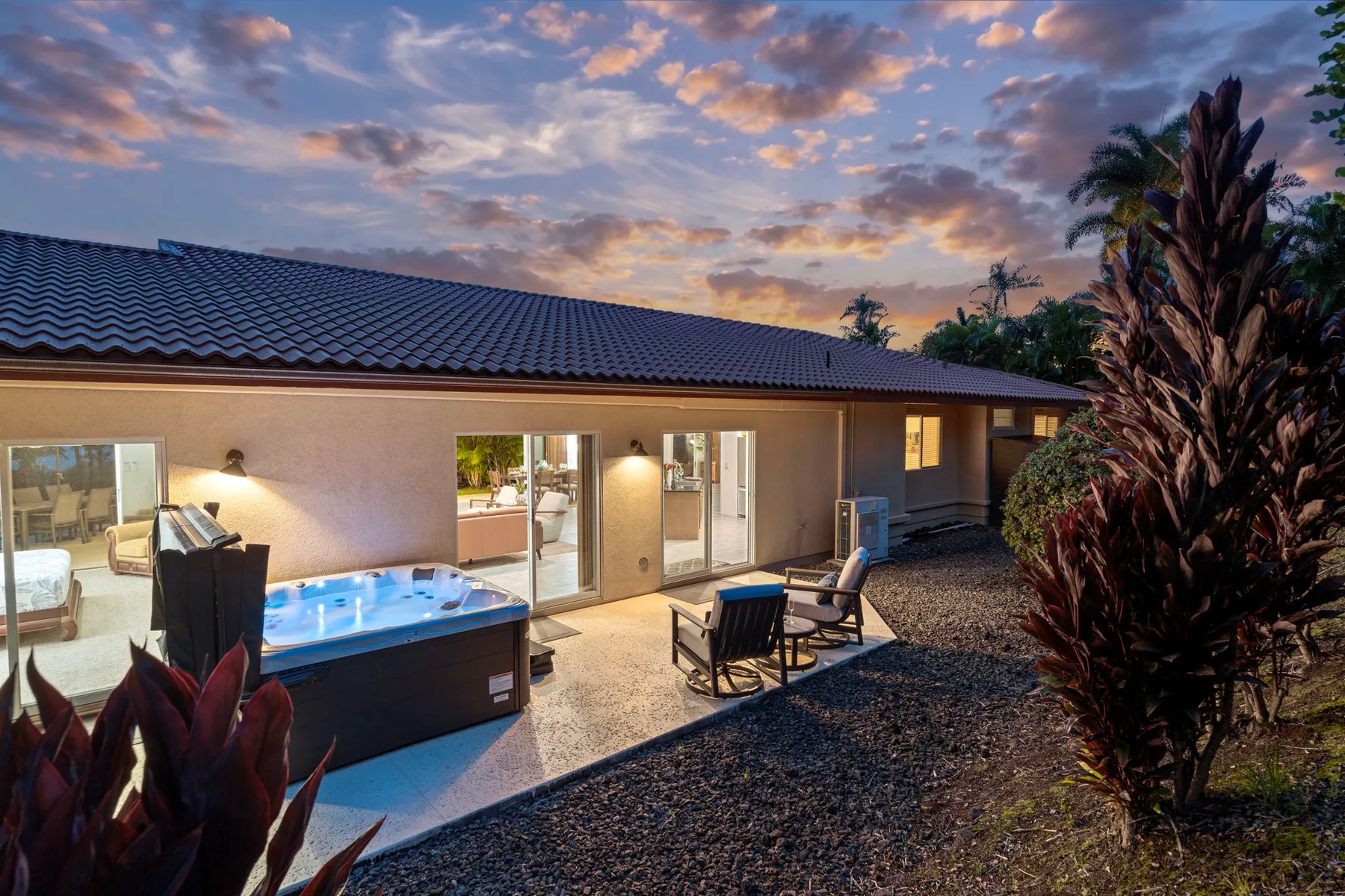 A modern house opens onto an outdoor patio with a lit hot tub at sunset.