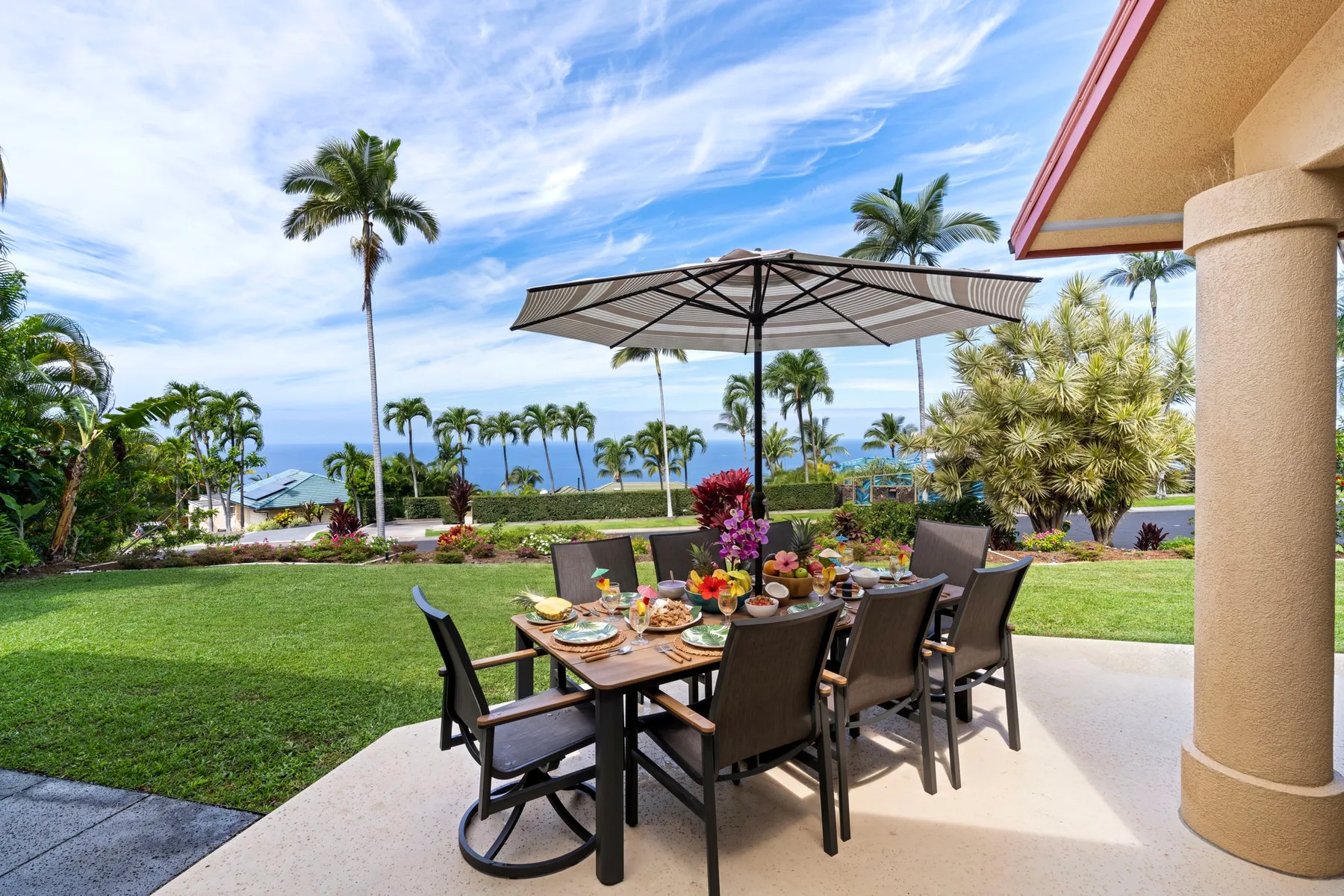 An outdoor dining area with a table beneath an umbrella overlooks a landscaped lawn.