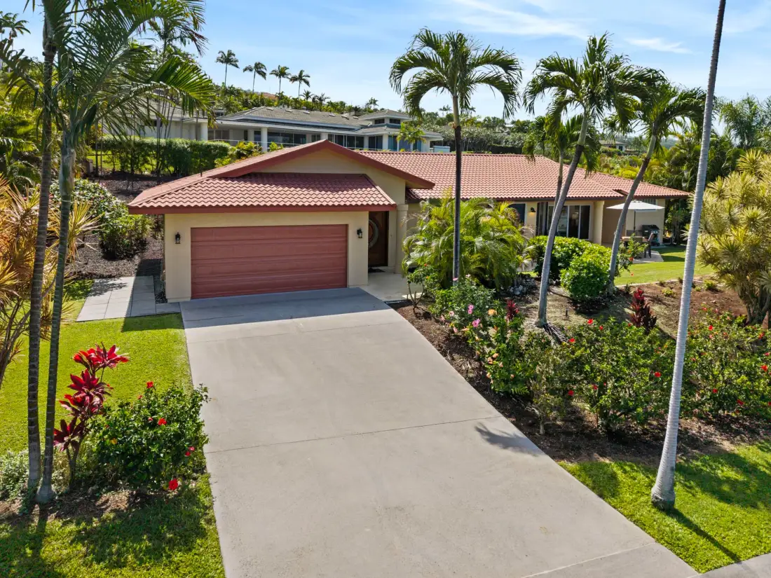 A single-story house with a red-tiled roof stands beside a landscaped driveway.