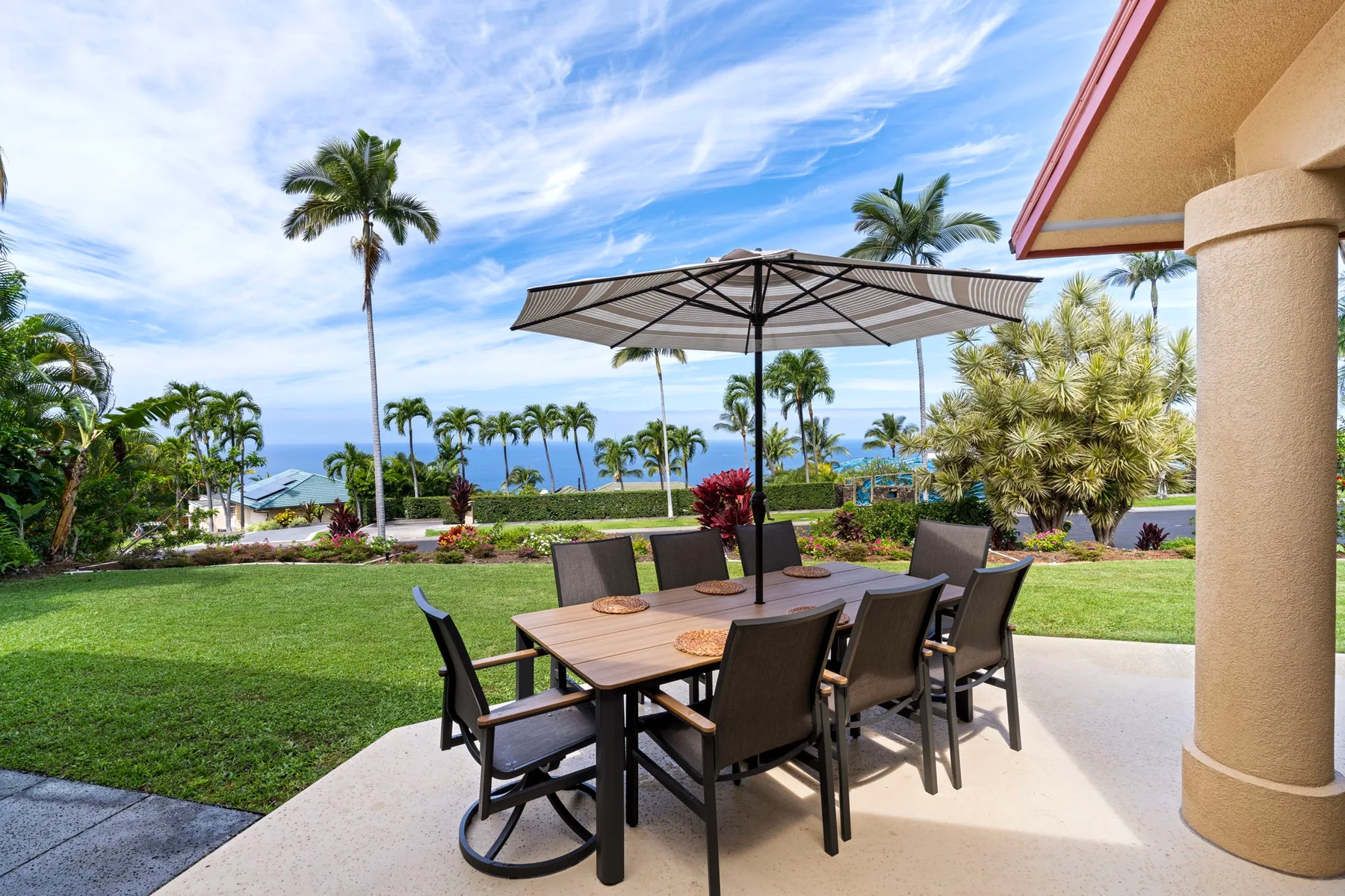An outdoor patio dining area overlooks a lawn and palm trees.