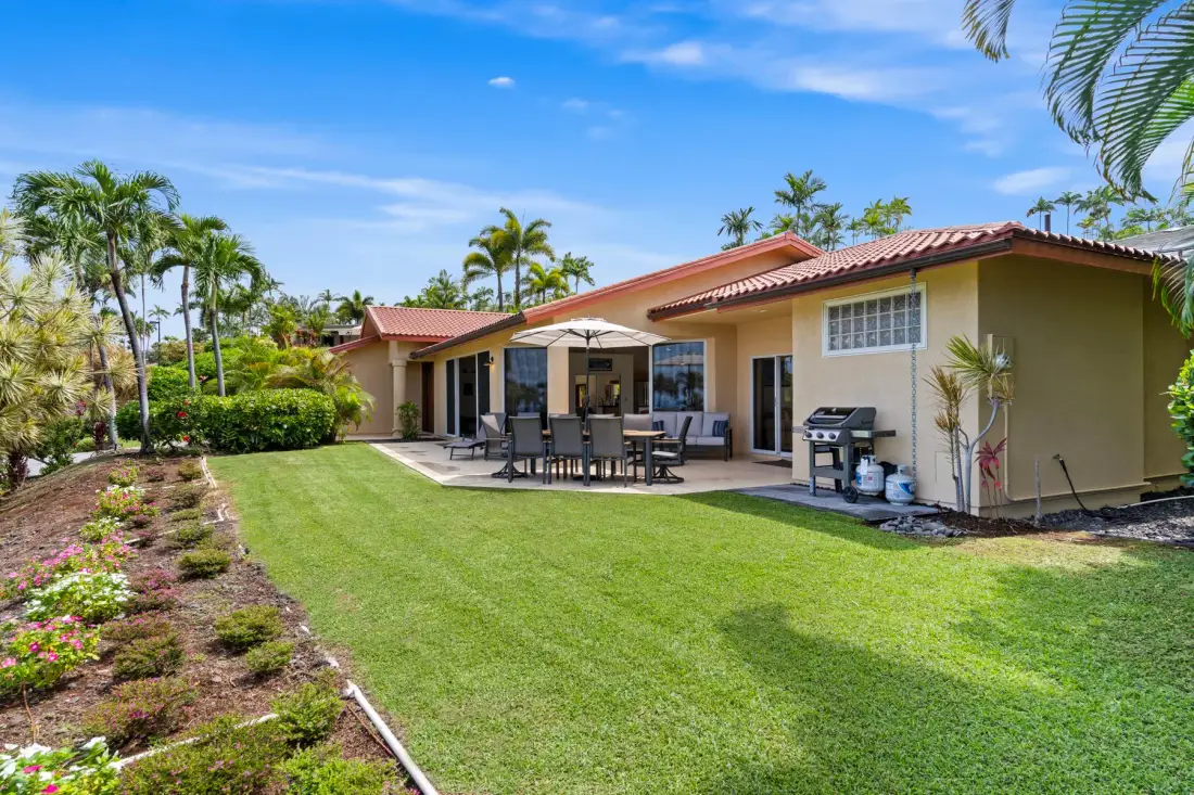 A house opens onto a green lawn and a patio with outdoor seating.