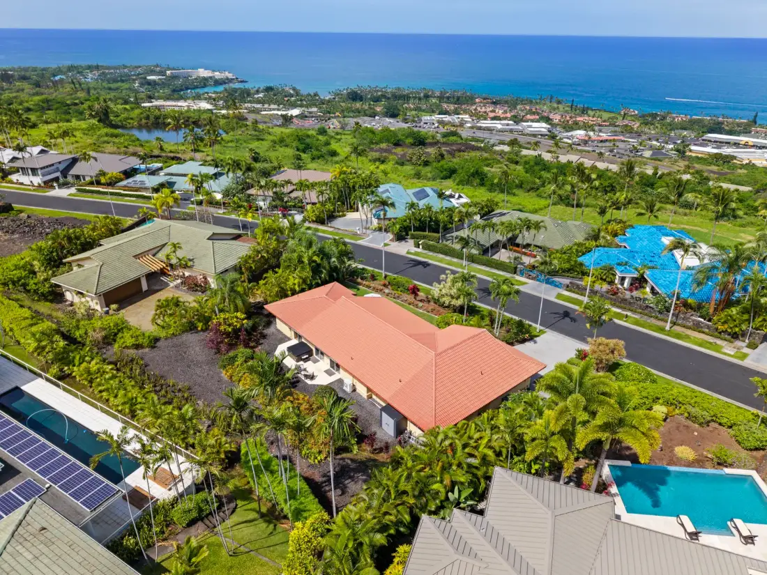 Aerial view of a tropical coastal neighborhood with homes, greenery, and the ocean.