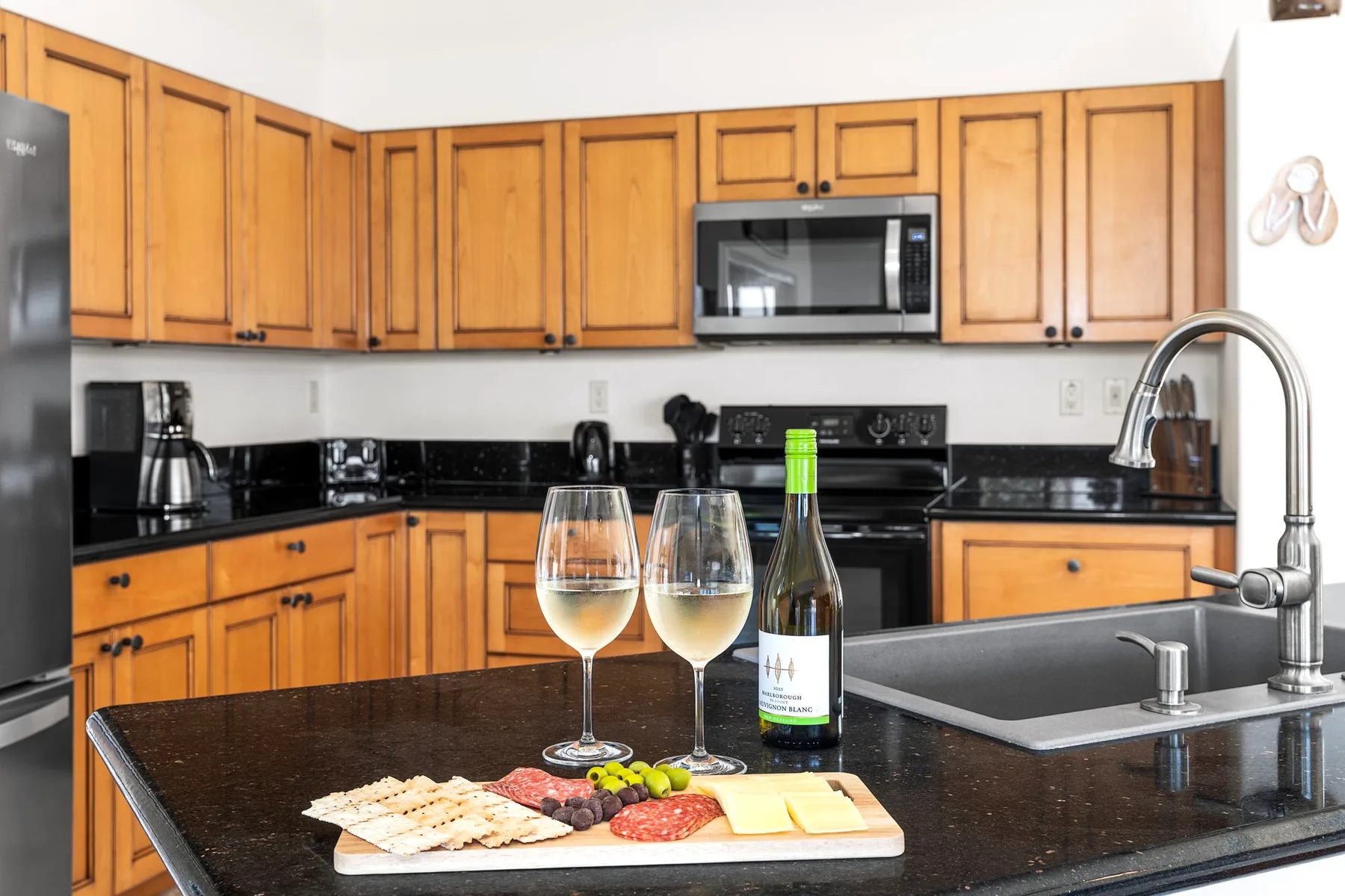 A kitchen with wooden cabinets and a countertop holding wine and snacks.