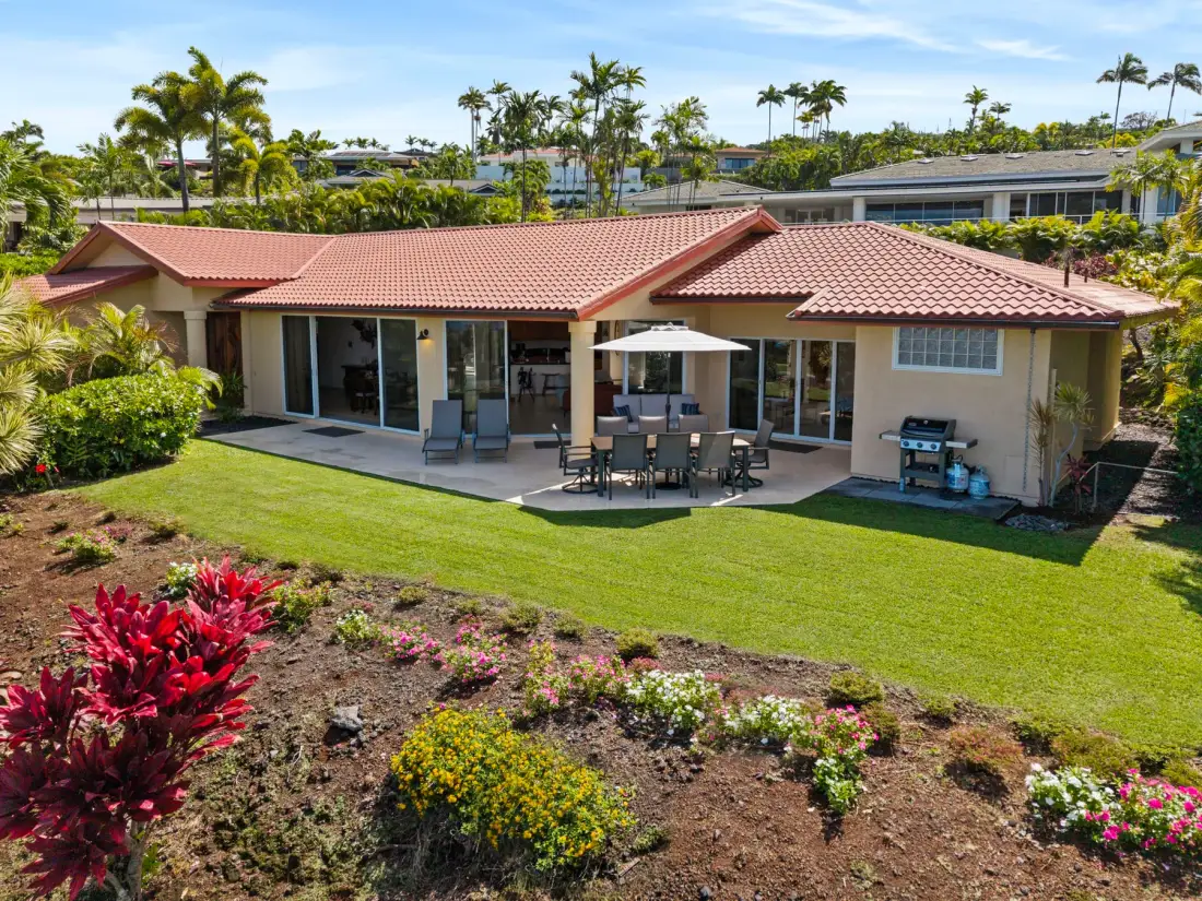 A single-story house opens onto a patio with outdoor seating and a green lawn.