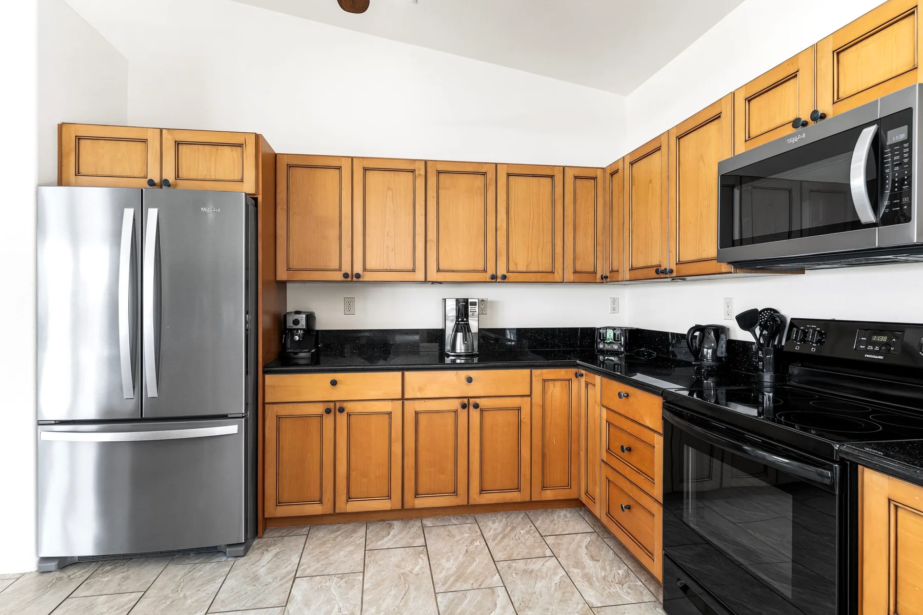 A kitchen with wooden cabinets, stainless steel refrigerator, and black appliances.