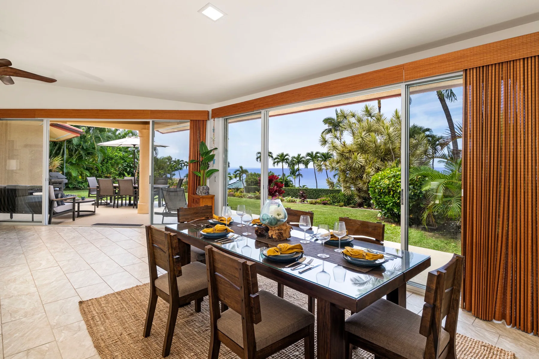 A dining area with a long table beside large windows overlooking a garden.