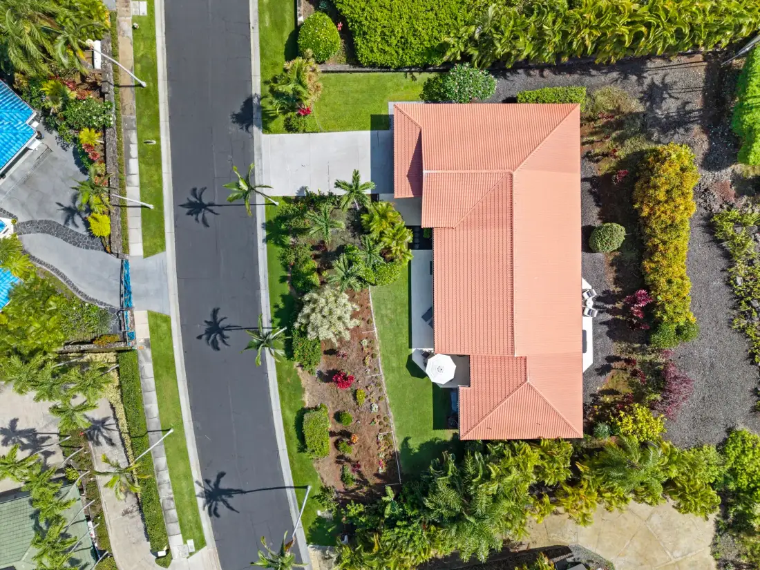 An aerial view shows a house with a red roof, gardens, and a road.