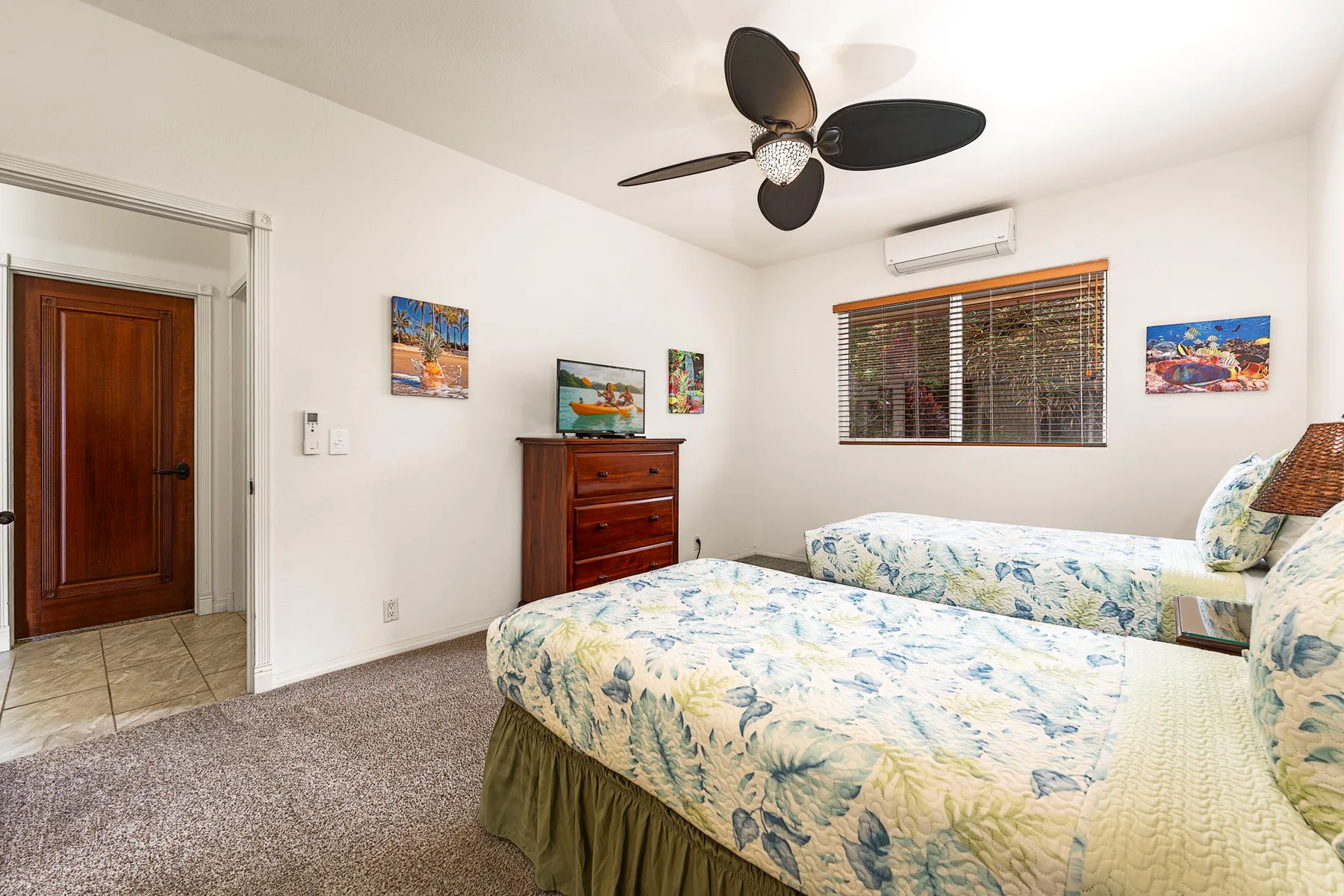 A bedroom with two beds, floral bedding, and a dresser beneath a television.