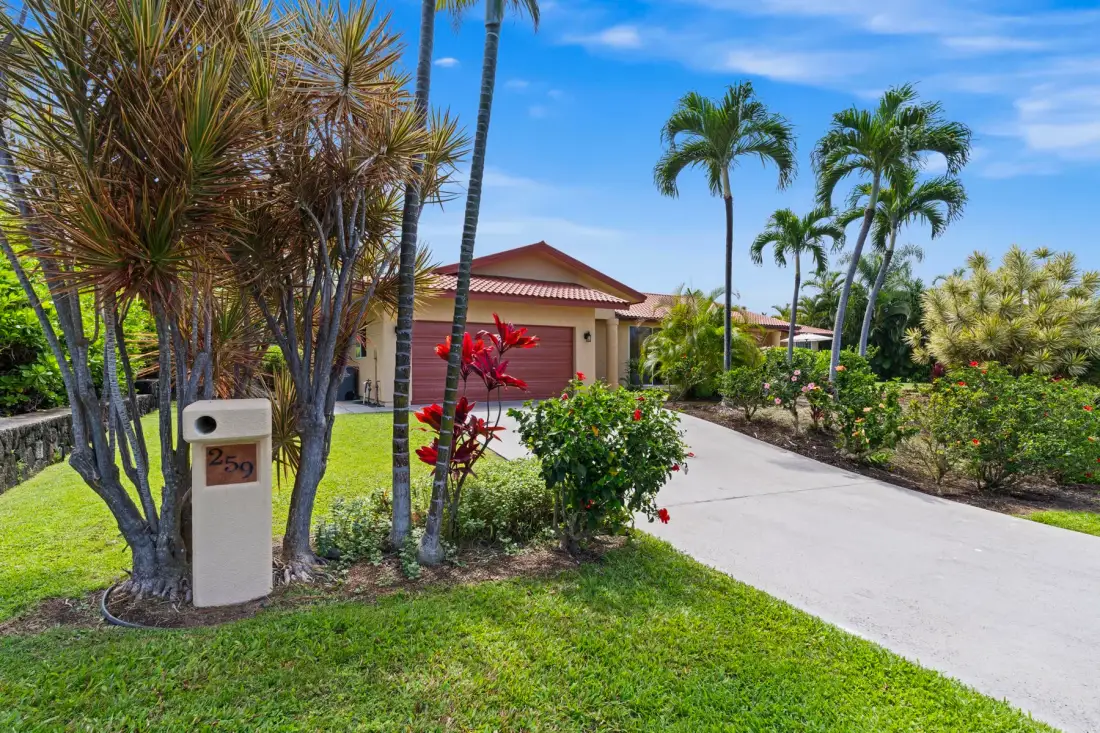 A landscaped driveway leads toward a house with a garage and palm trees.