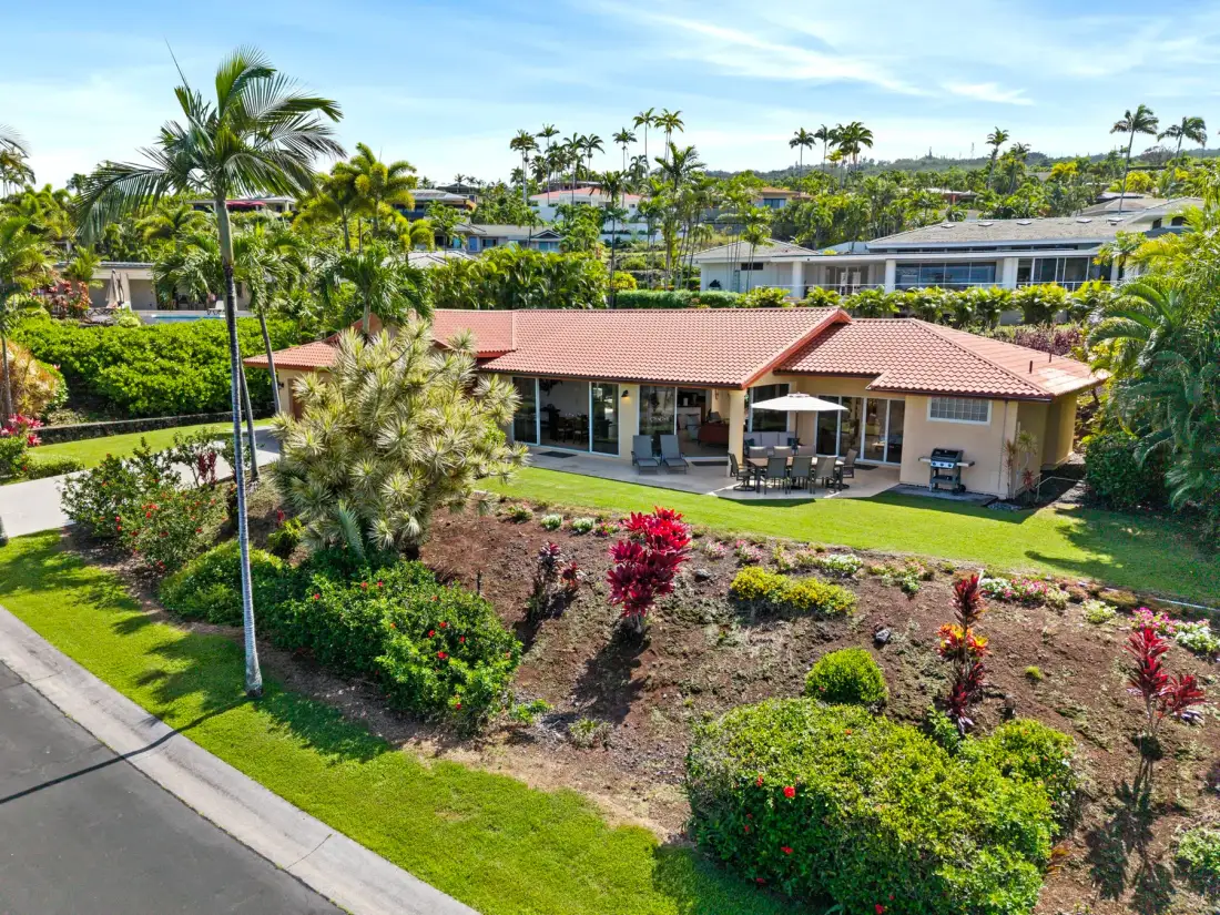 A single-story house with a red-tiled roof sits among landscaped gardens.