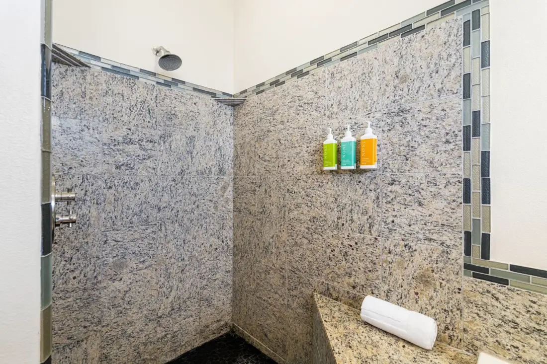 A tiled shower area with wall-mounted dispensers and a folded towel.