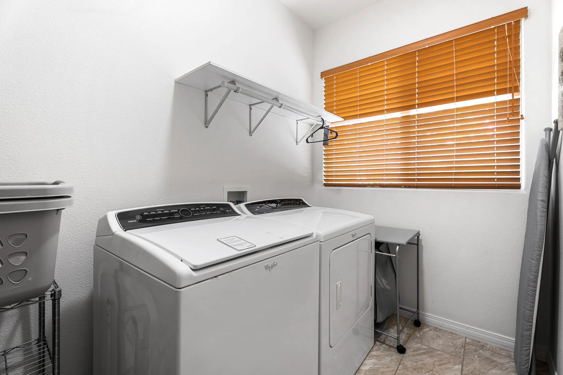 A laundry room with a washer and dryer beneath a window with wooden blinds.