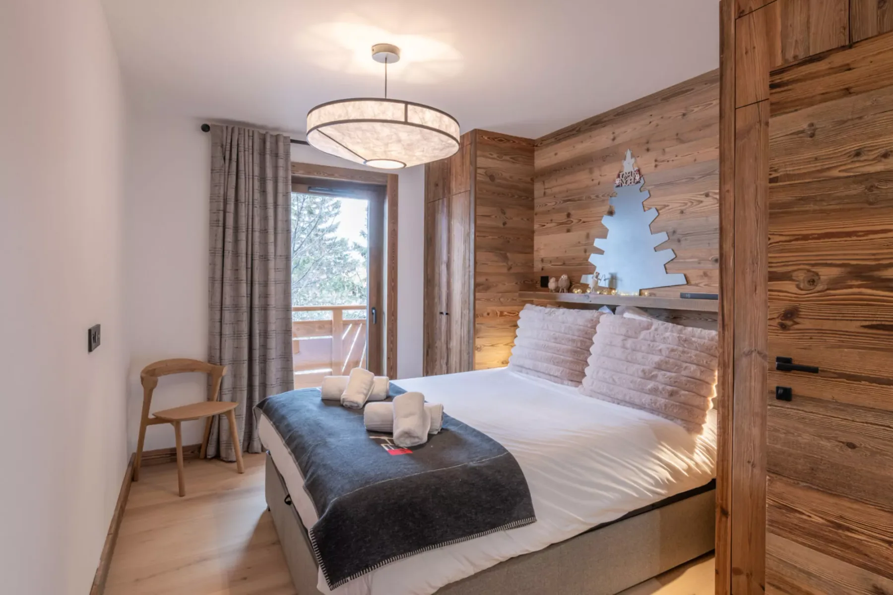 A bedroom with a bed, wood-paneled walls, and a glass door opening to a balcony.