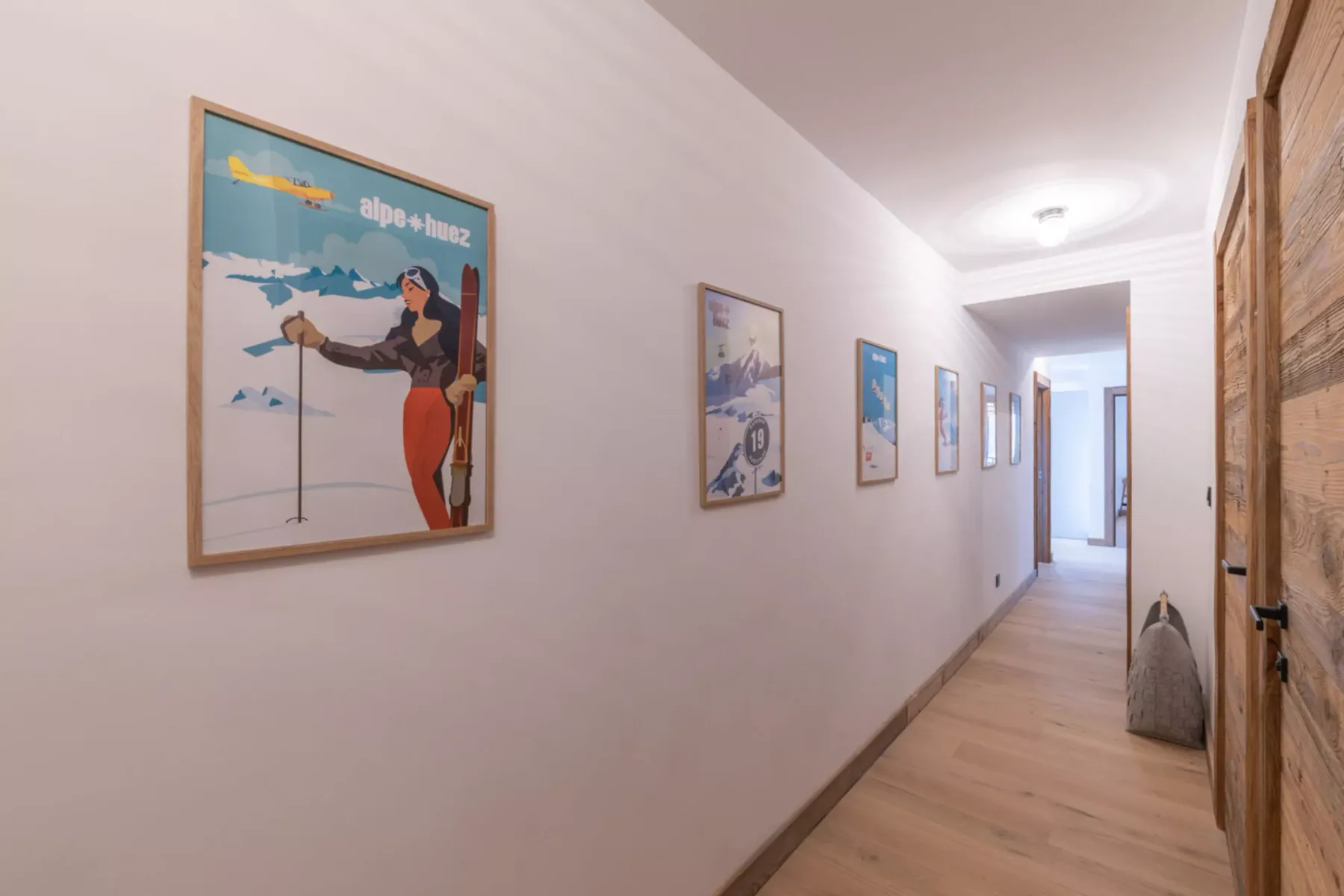 A hallway with framed artwork along the wall and a wooden door.