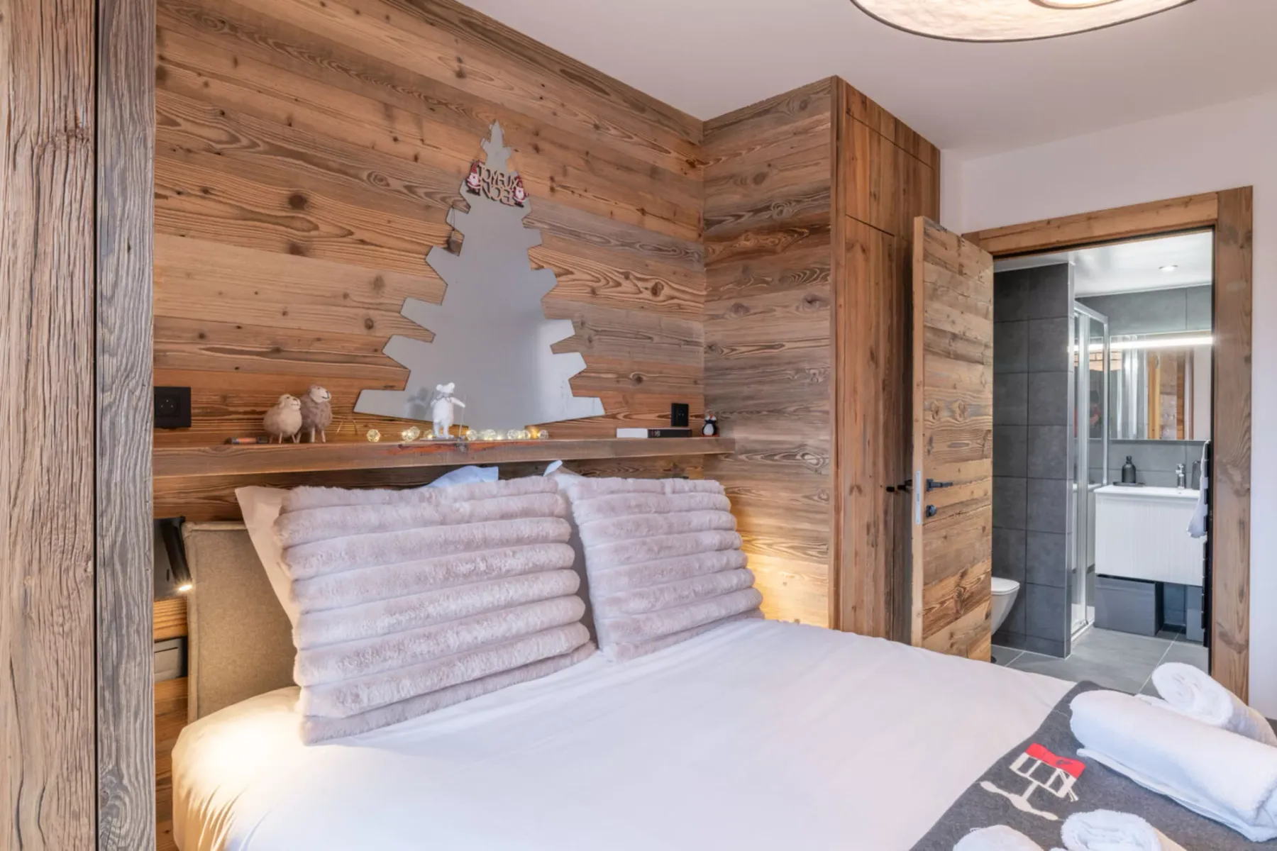 A bedroom with a bed and wood-paneled walls, with an open doorway to a bathroom.