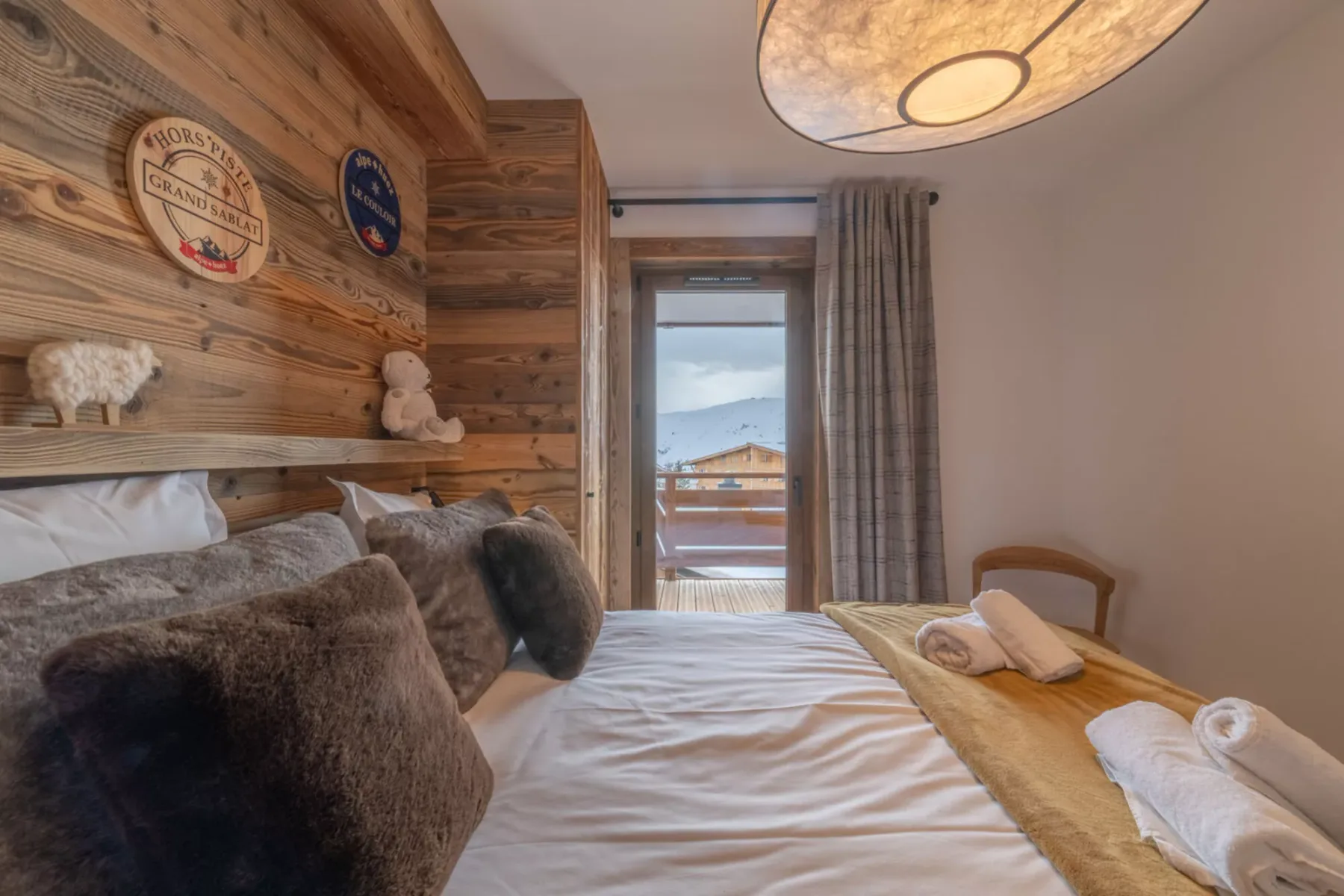A bedroom with a bed, wooden wall paneling, and a glass door opening onto a balcony.