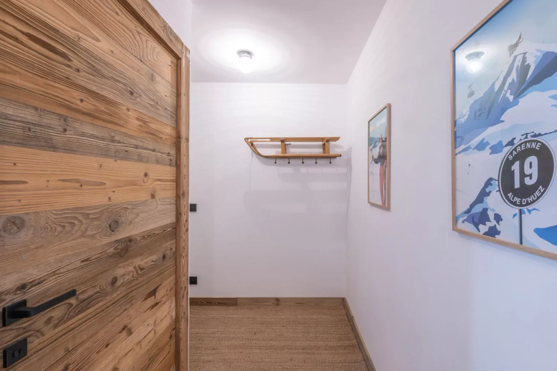 A narrow entry hallway with a wooden door, wall shelf, and framed prints.