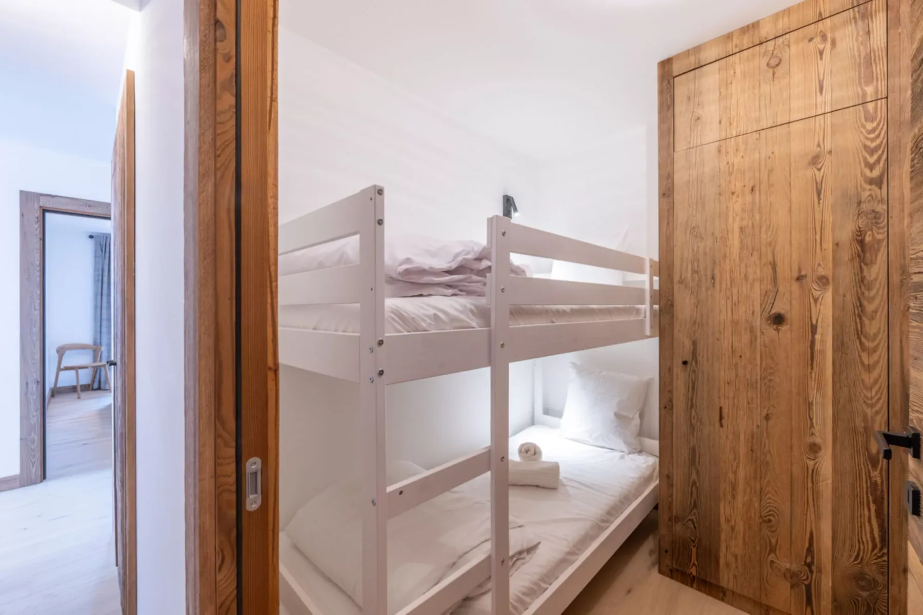 A bunk-bed sleeping area with white bedding and a wooden door.